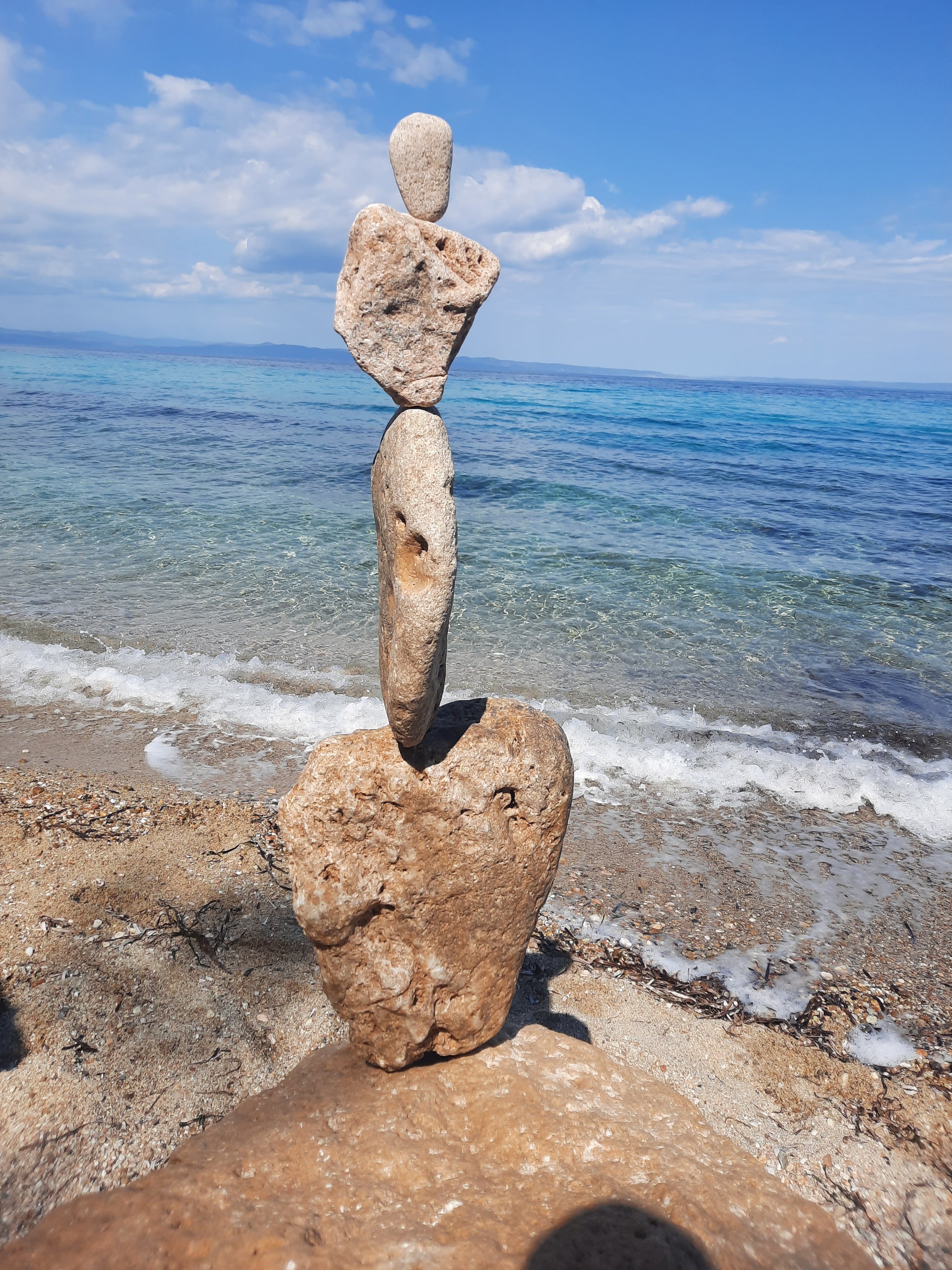 Steinmännchen aus vier Steinen auf einem Strand mit Blick auf das Meer und Himmel mit Wolken.