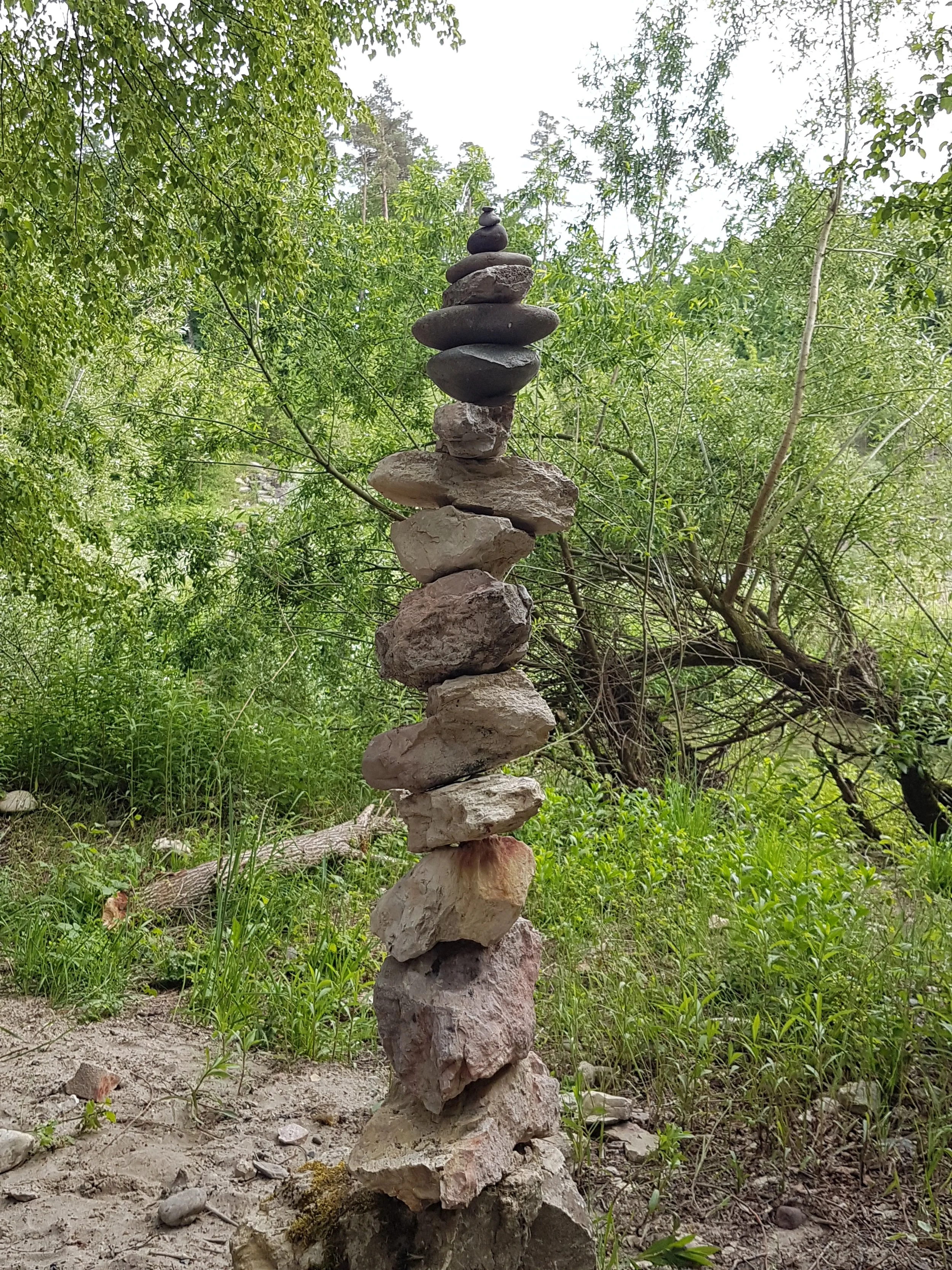 Ein Turm aus verschiedenen flachen Steinen und Felsen, auf einem Boden in einem bewaldeten Gebiet.