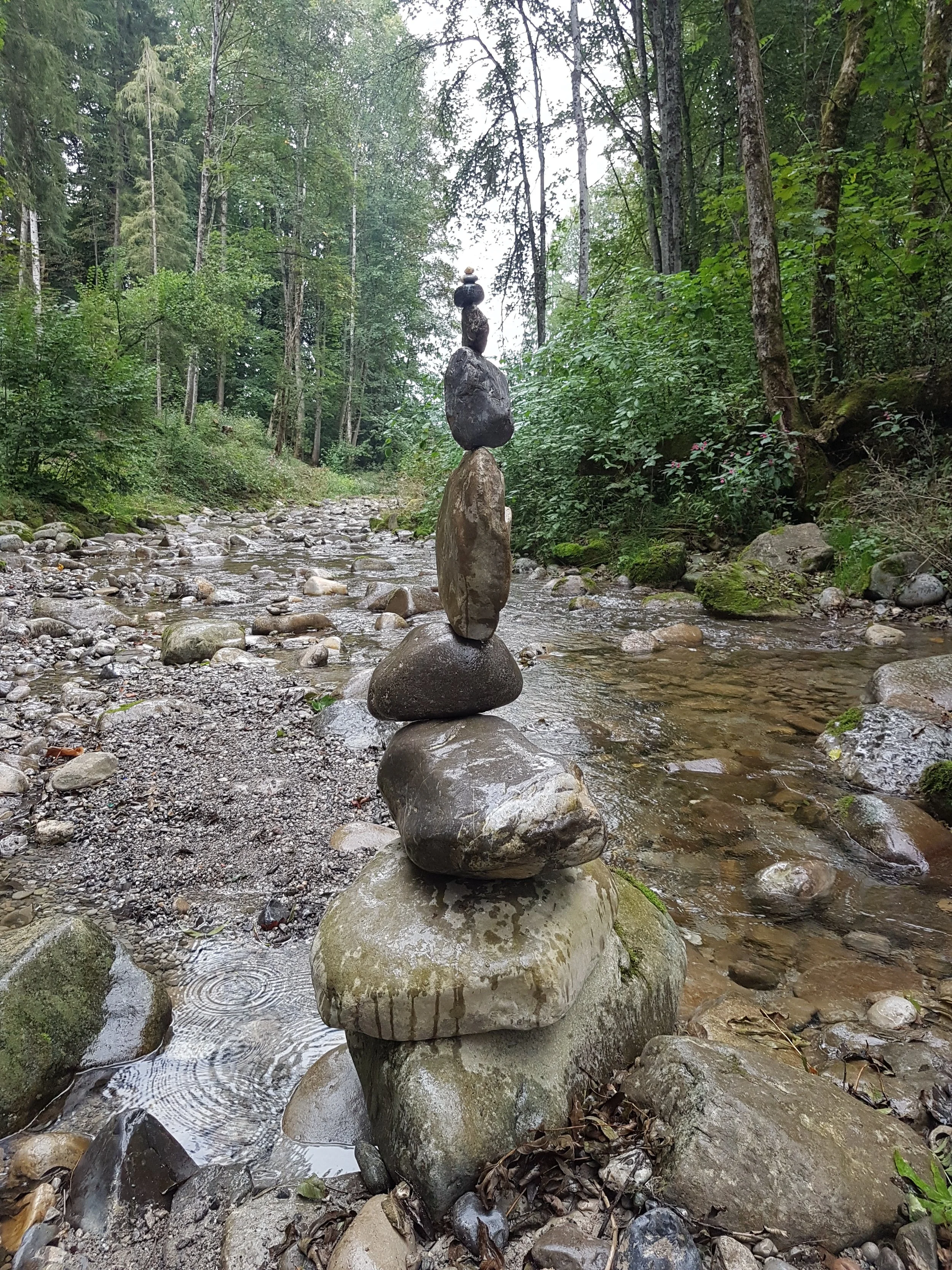 Steinkunst im Fluss in einem Wald, bestehend aus mehreren Steinen, die aufeinander gestapelt sind.