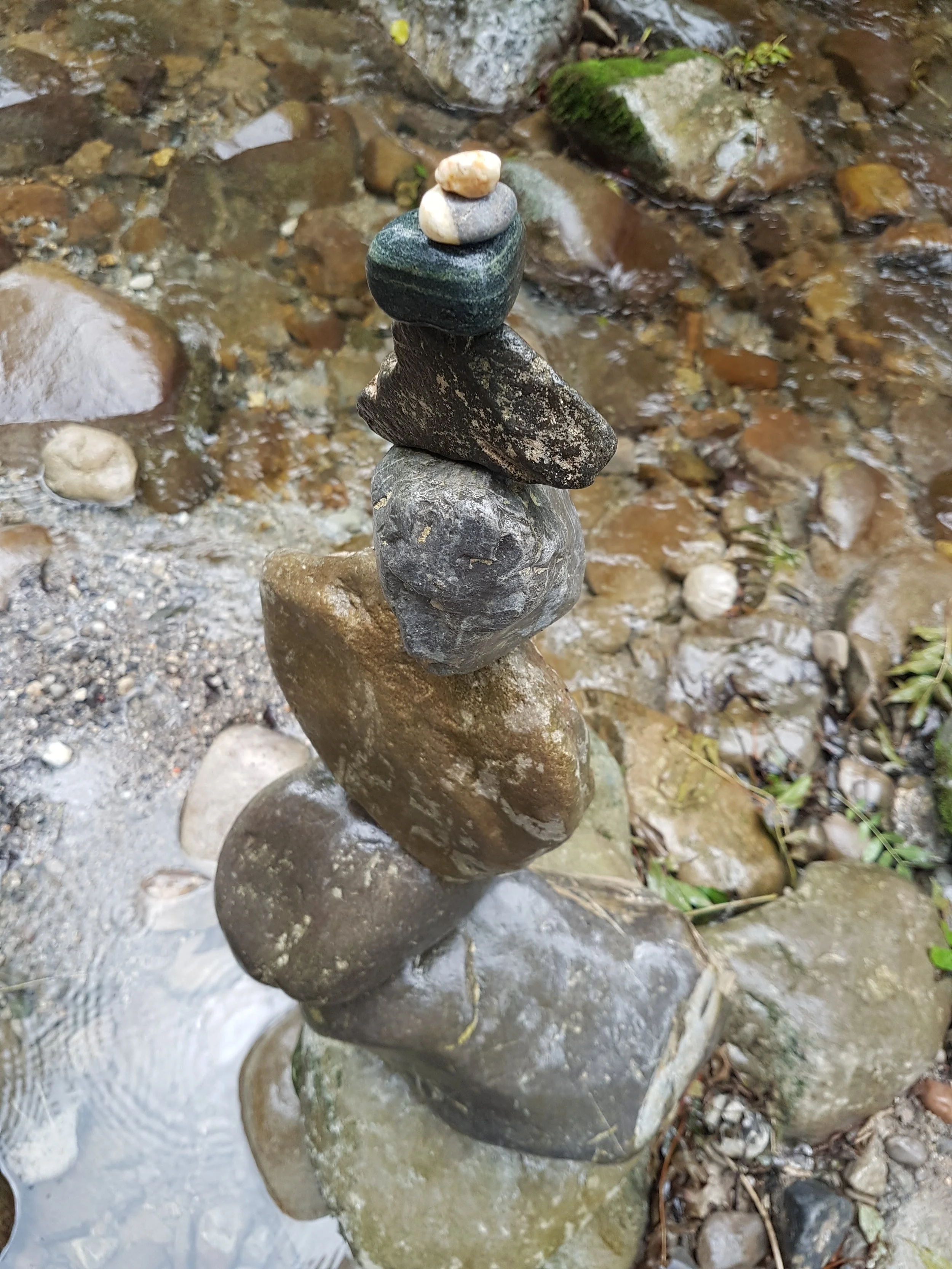 Fünf Steine in einer Wackelbrücke auf einem Bachbett gestapelt, um eine Skulptur zu bilden.