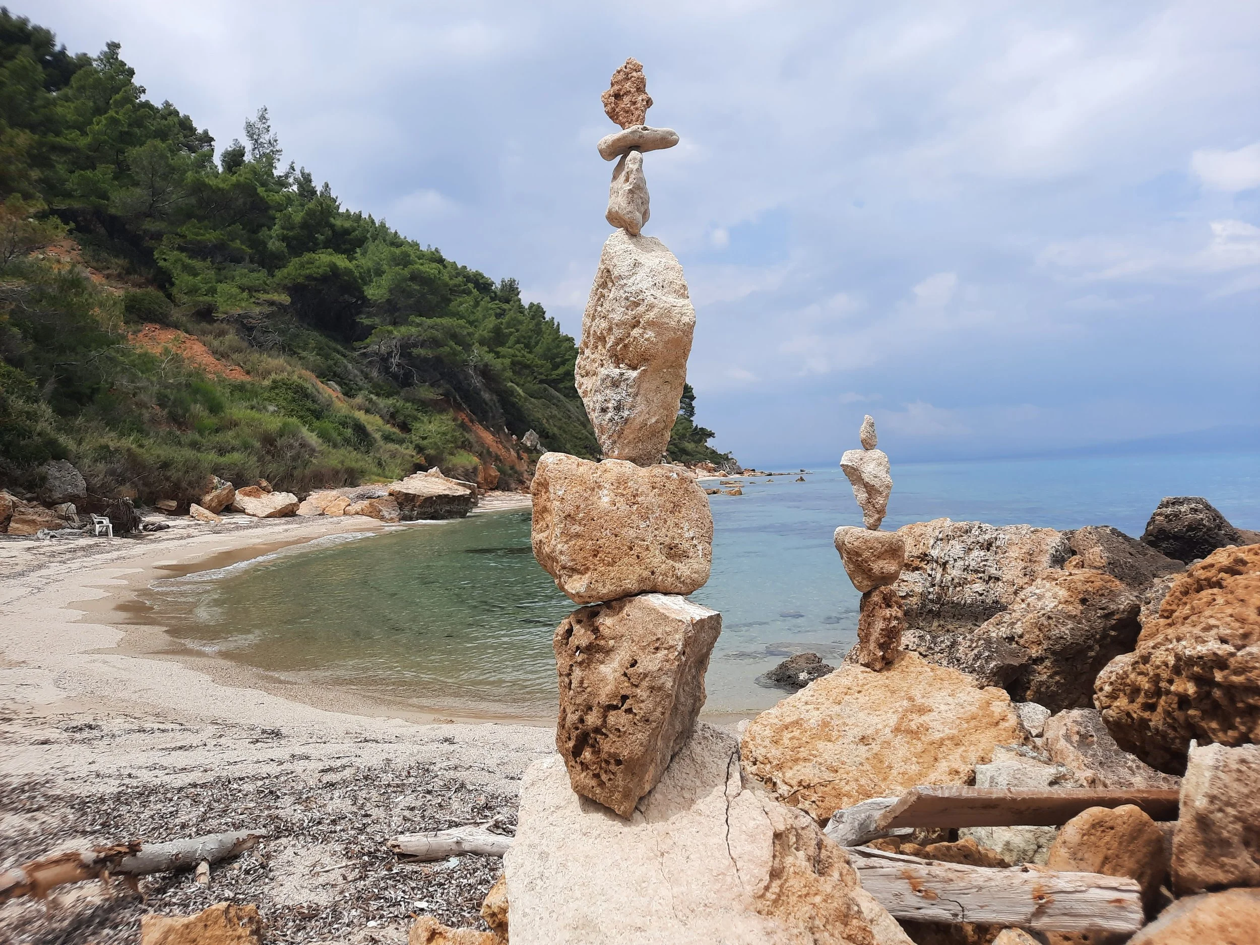 Kunstvolle Steinsäulen am Strand mit Meeresblick und bewaldeten Hügeln im Hintergrund.