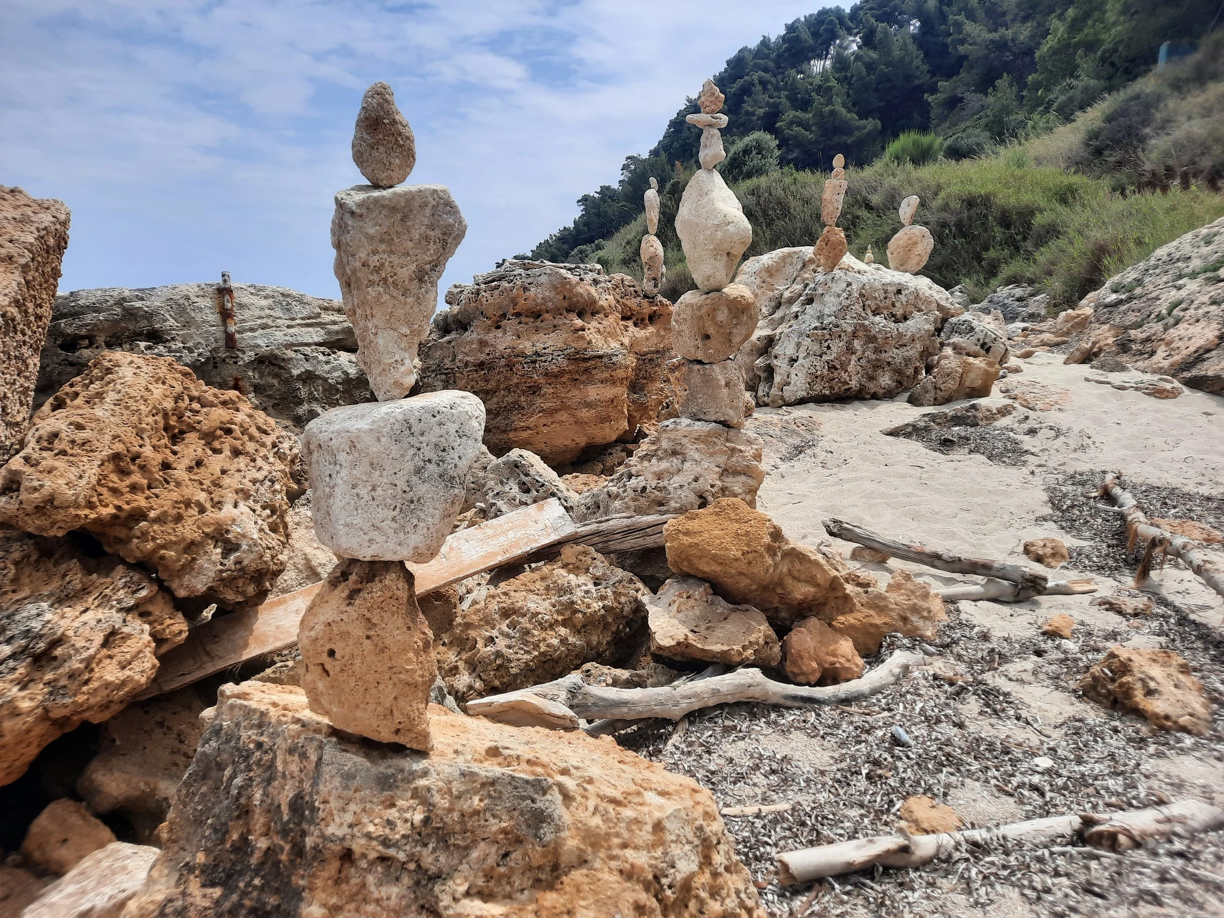 Steine und kleine Steintürme am Strand, im Hintergrund Bäume und Himmel