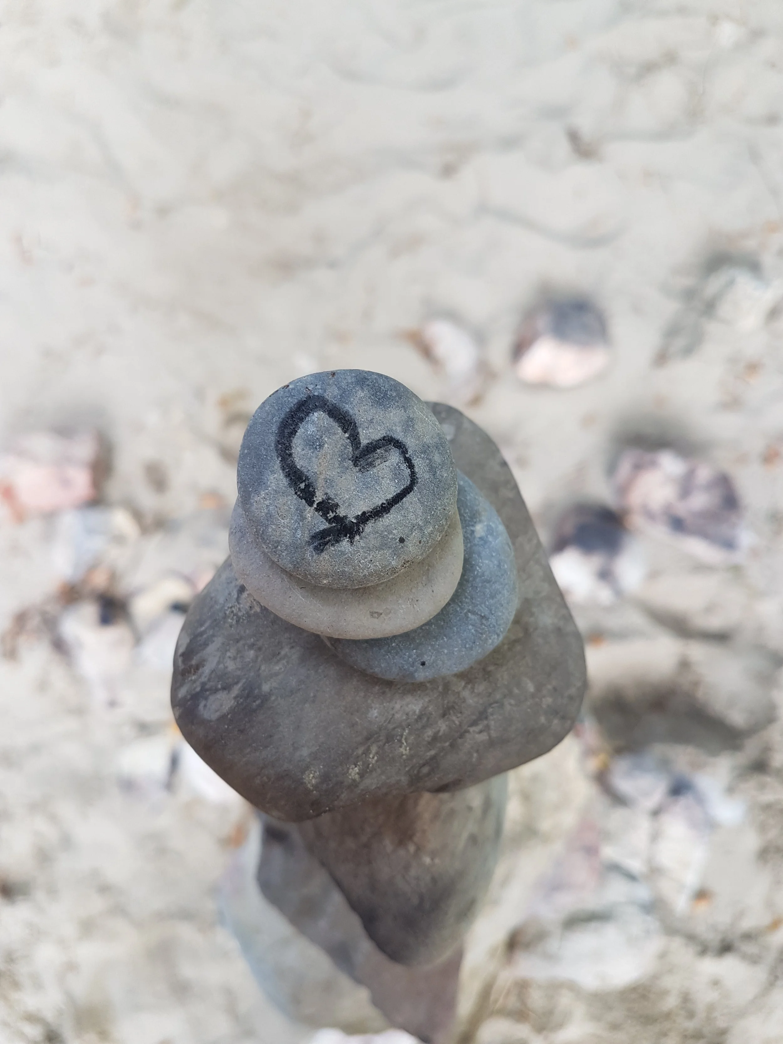 Fünf Steine aufeinander gestapelt, auf dem obersten Stein ist ein Herz gemalt.