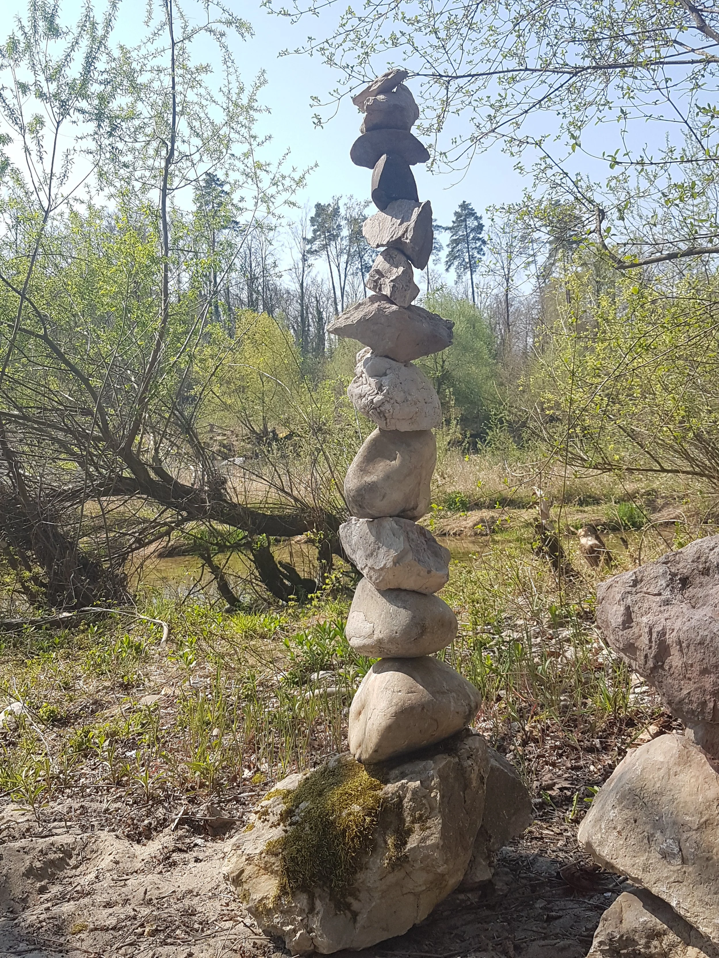 Felsen in einer natürlichen Umgebung, die zu einem Turm gestapelt sind, im Freien bei Sonnenlicht, mit Bäumen im Hintergrund.