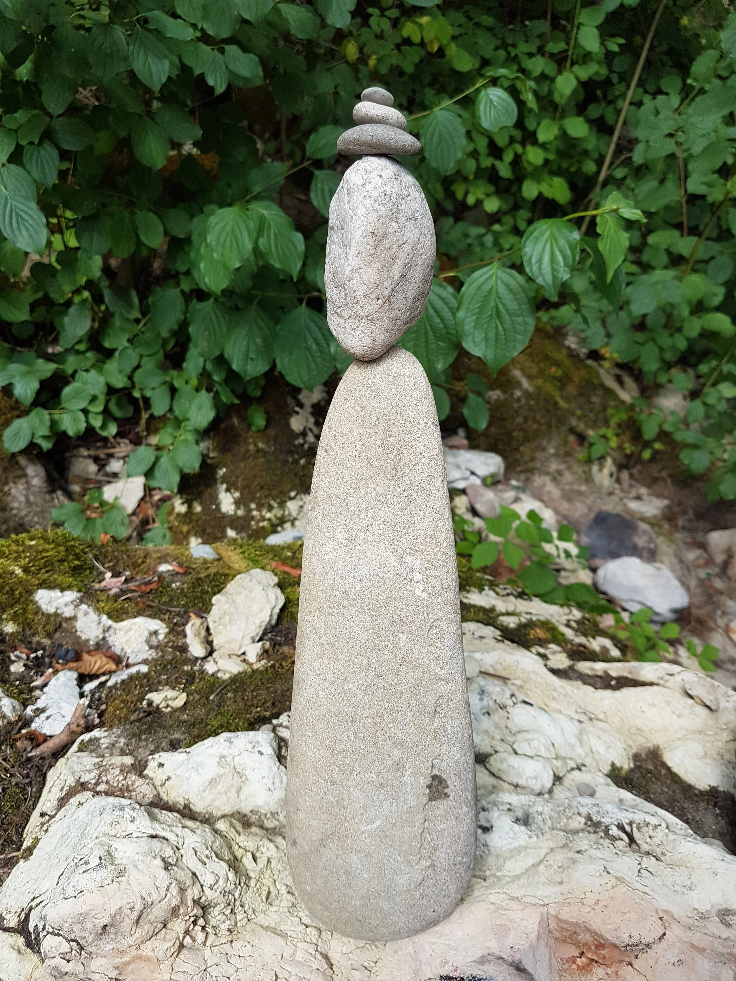 Steinmännchen aus mehreren Steinen auf einem Felsen, im Hintergrund grüne Blätter.