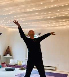 Person standing with arms raised in a peaceful room with string lights on the ceiling