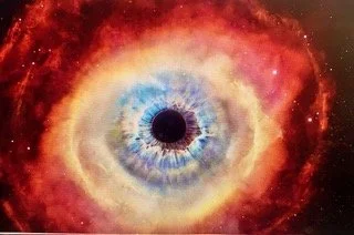 Close-up of a blue human eye with outer space, stars, and a nebula reflected in the iris.