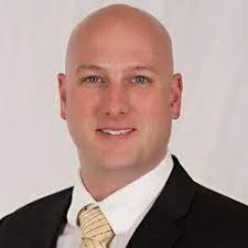 Headshot of a bald man wearing a suit and tie, smiling against a light background.