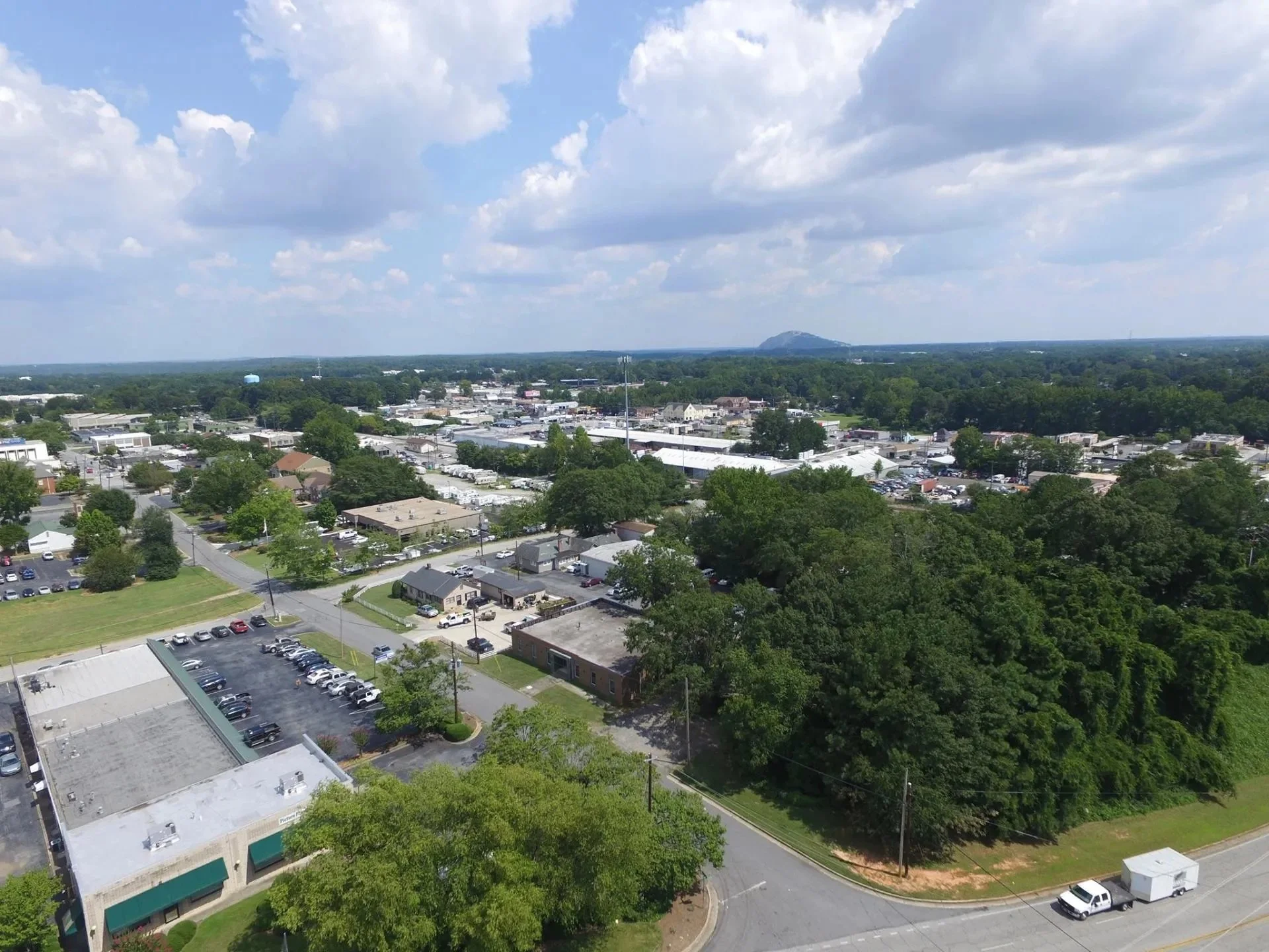 Aerial view of a suburban area with a mix of residential, commercial, and green spaces, under a partly cloudy sky.