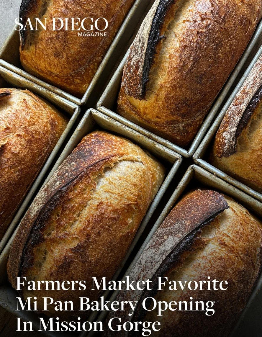 Close-up image of freshly baked loaves of bread with a golden-brown crust in metal trays, promoting a bakery opening in Mission Gorge.