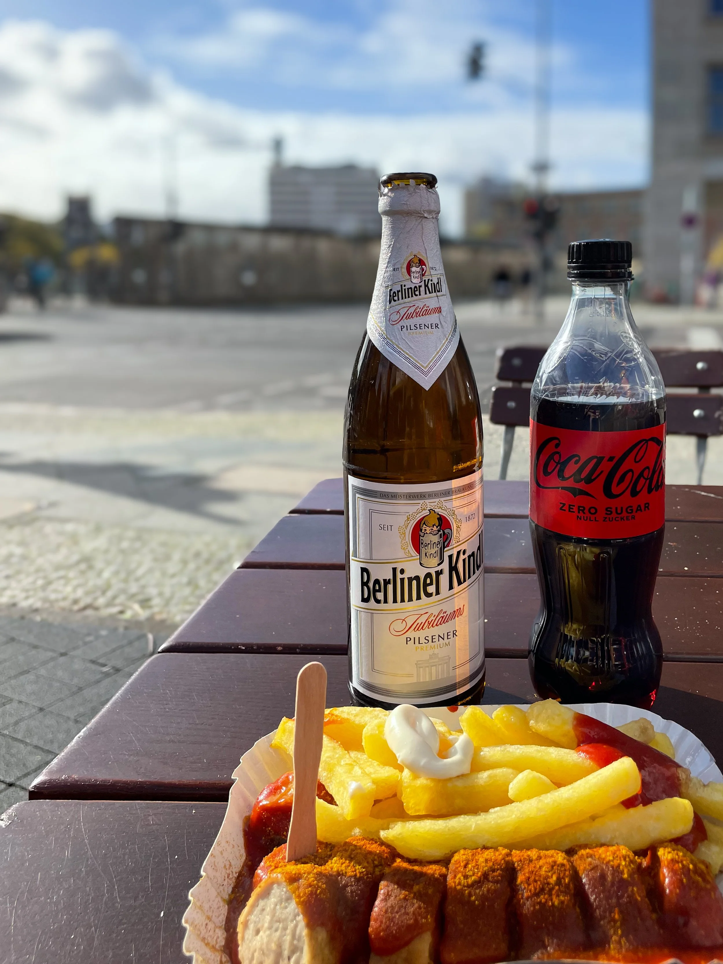currywurst, a beer and a coca cola in front of a part of the Berlin wall
