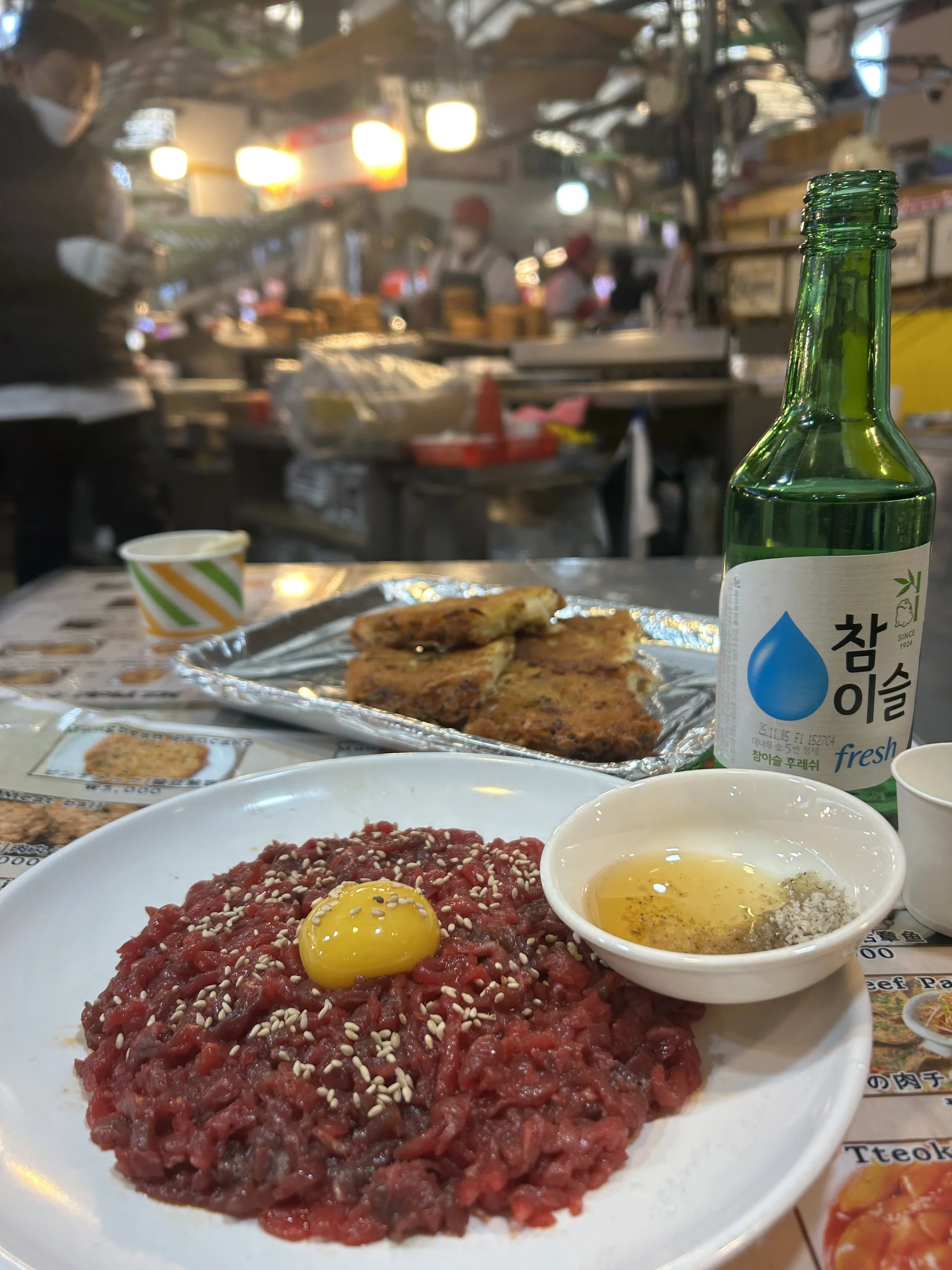 plate of beef tartare with raw egg and bottle of soju
