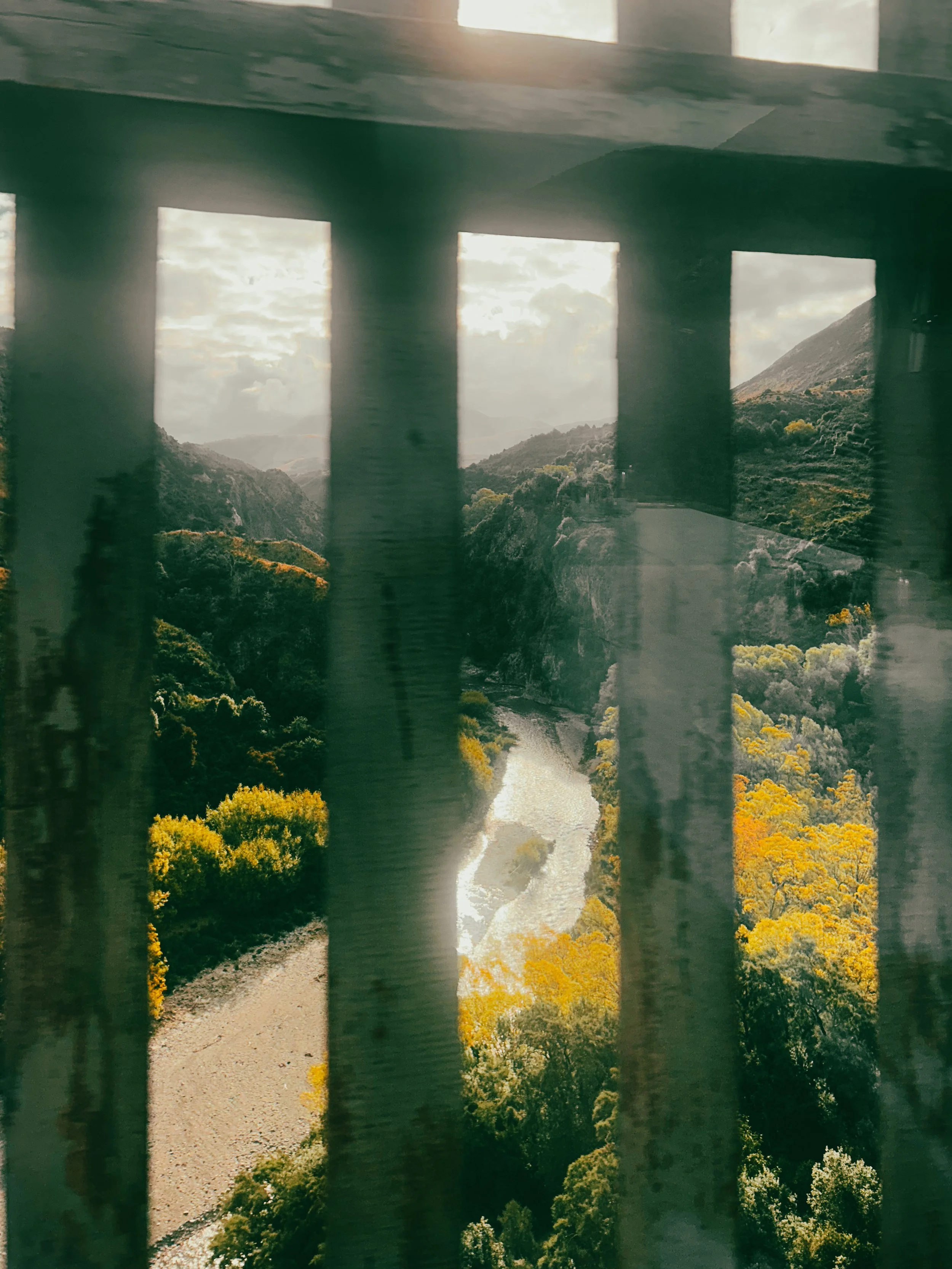 a river in the valley below a bridge as seen through the window of the TranzAlpine train