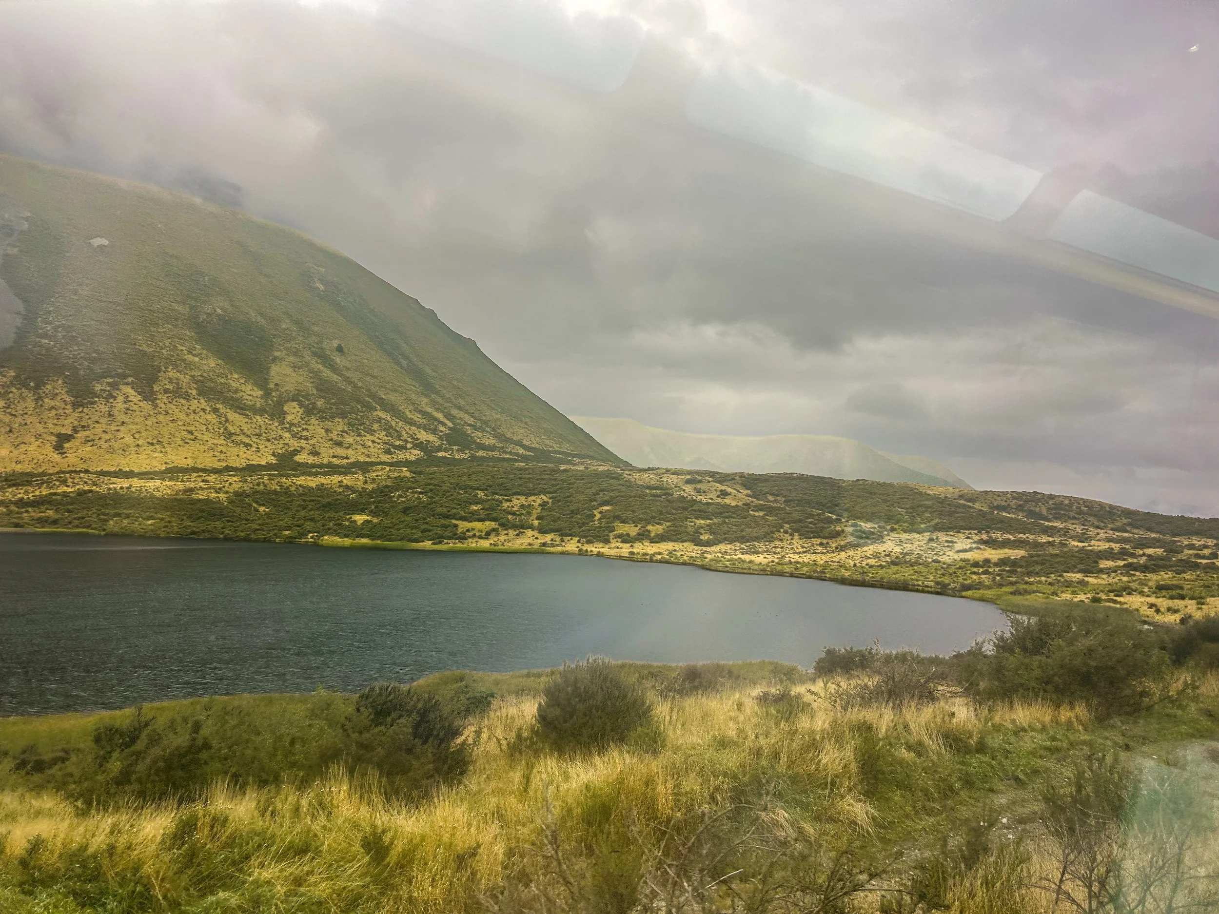 a foggy view outside the TranzAlpine train, with mountains and a lake