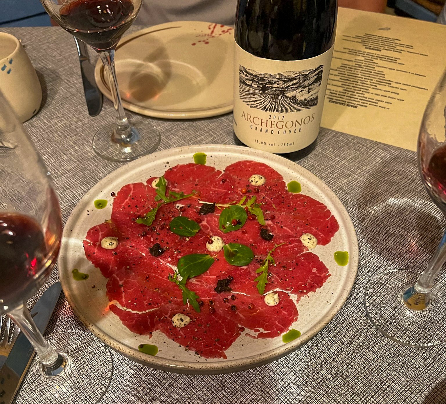 plate of beef carpaccio and bottle of Greek wine at Roka in Oia, Santorini