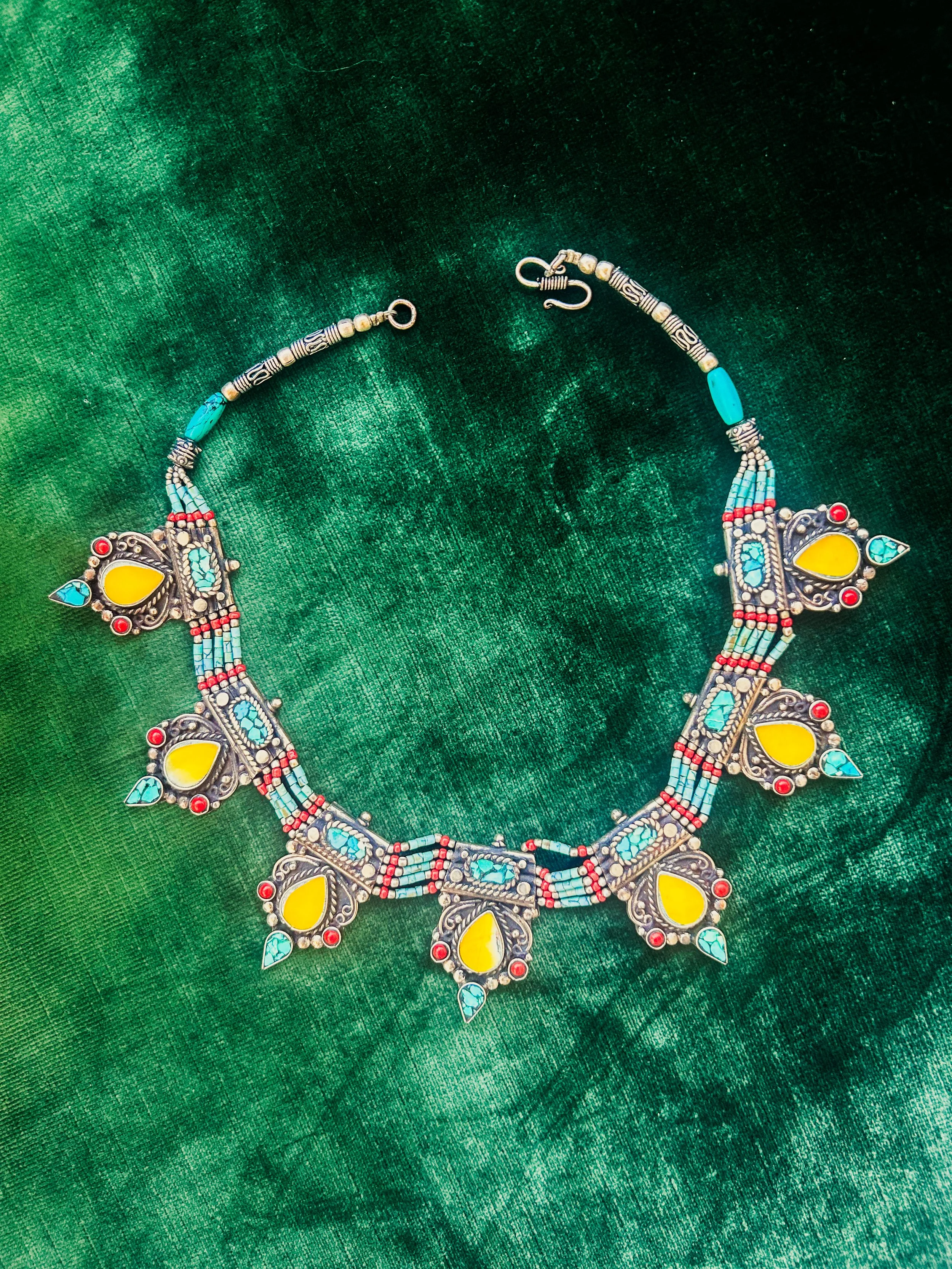 Silver Necklace with yellow, red and turquoise stones sitting on top of green velvet