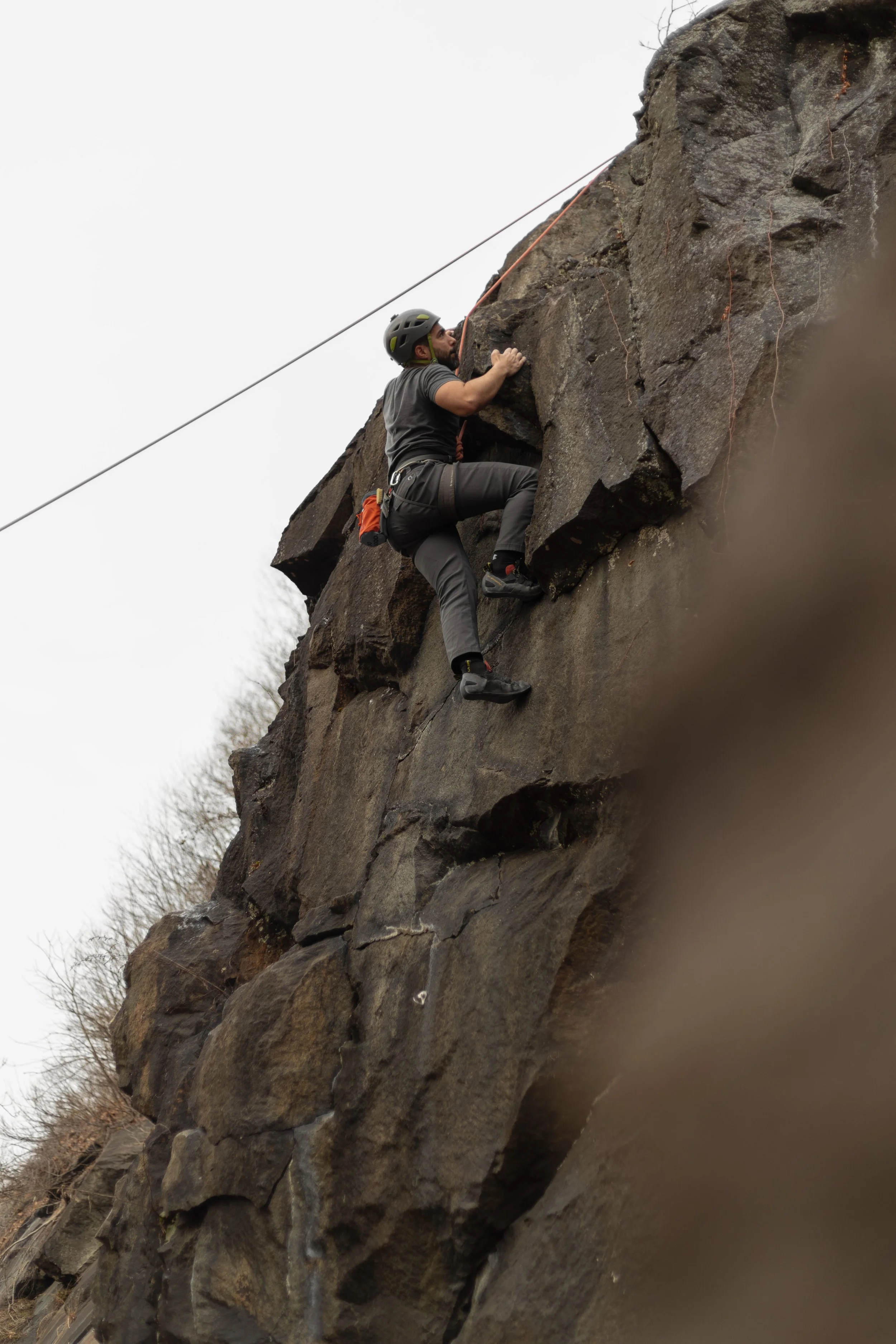 Man climbing a steep rock face while wearing a helmet and safety gear.