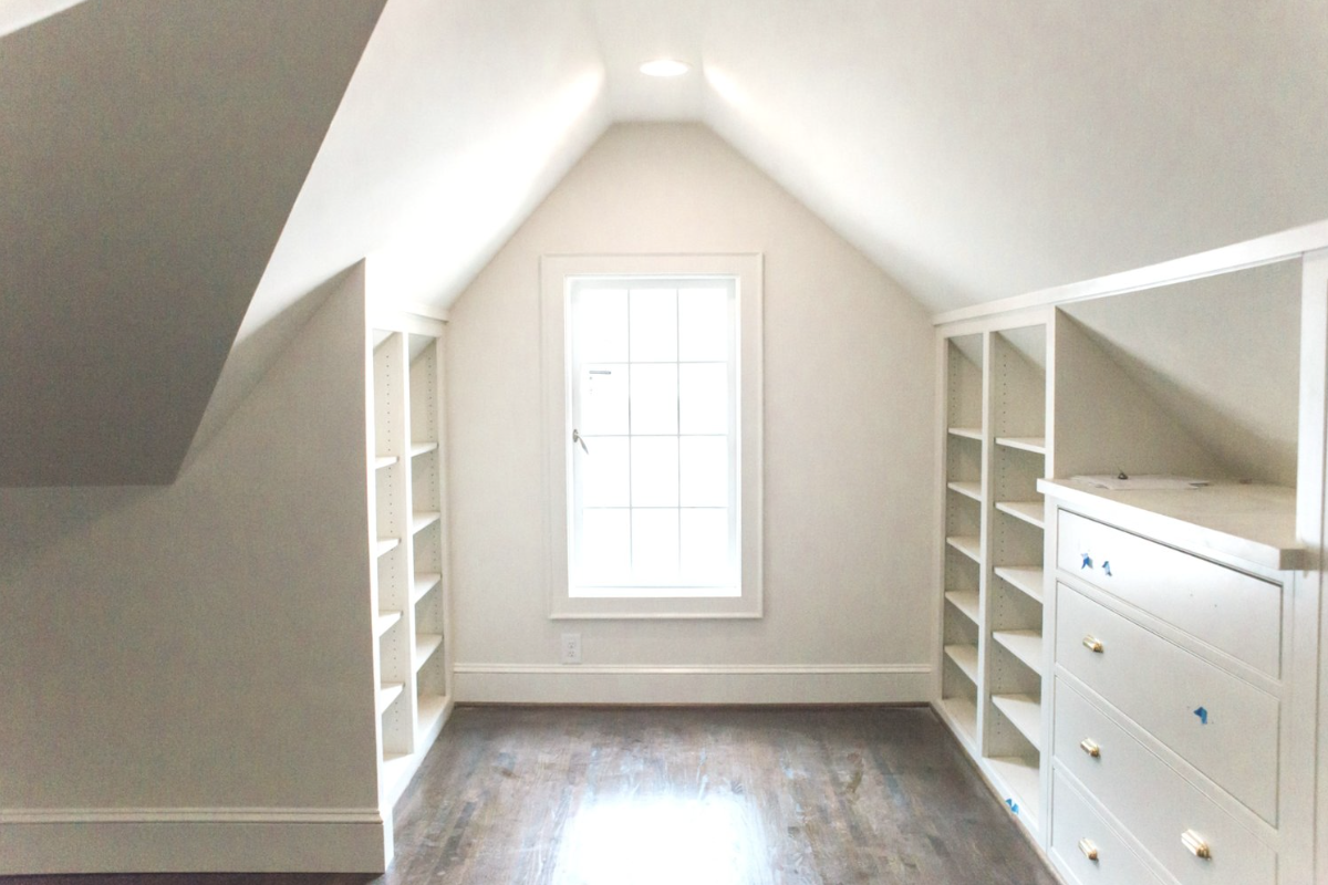 Empty room with white built-in shelves and dresser, wooden floor, and sloped ceiling with a window.