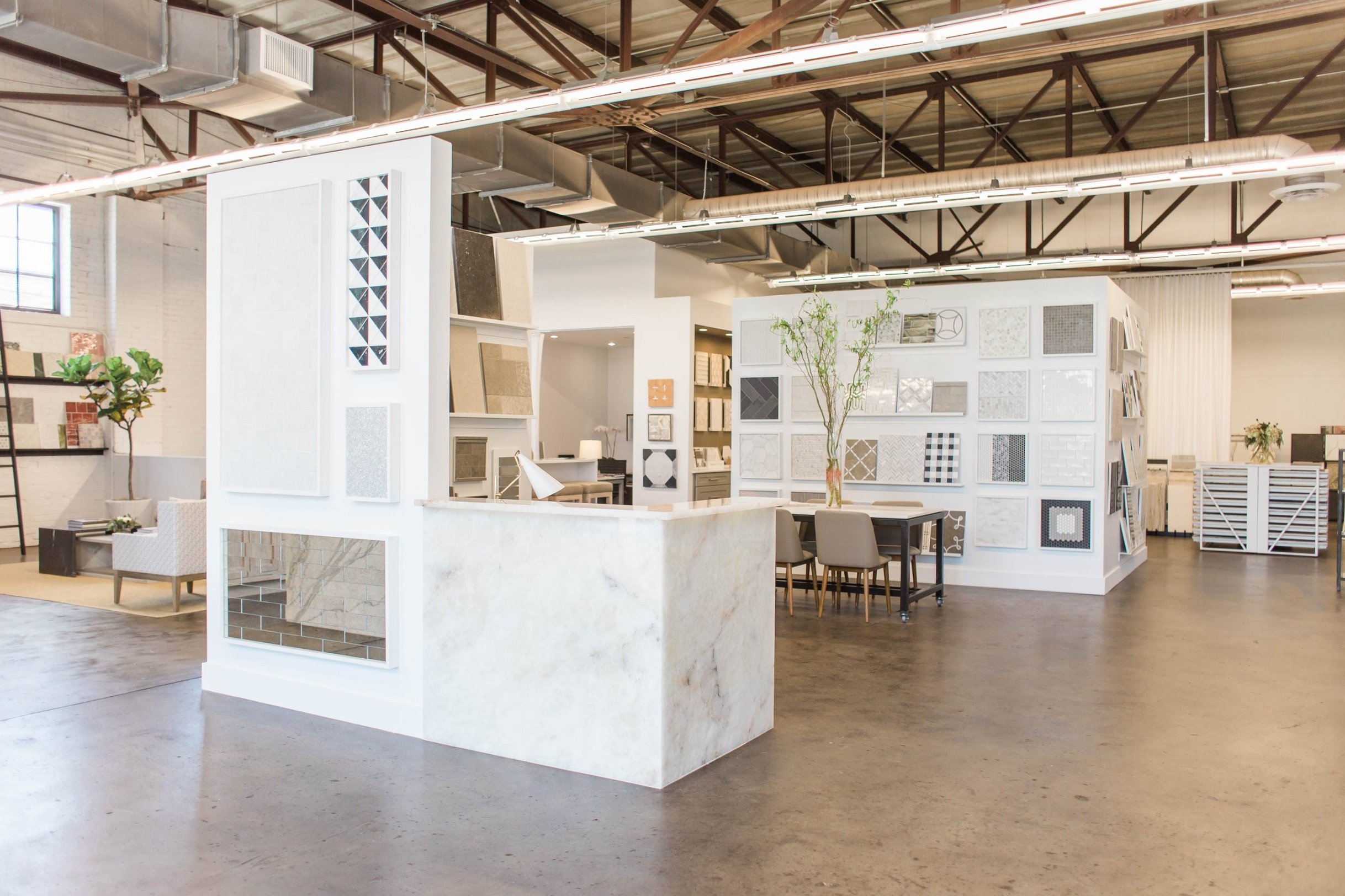 Interior of a modern tile showroom featuring walls adorned with various tile samples, a marble counter, seating area with chairs, and exposed ceiling beams. Downtown Birmingham, AL.