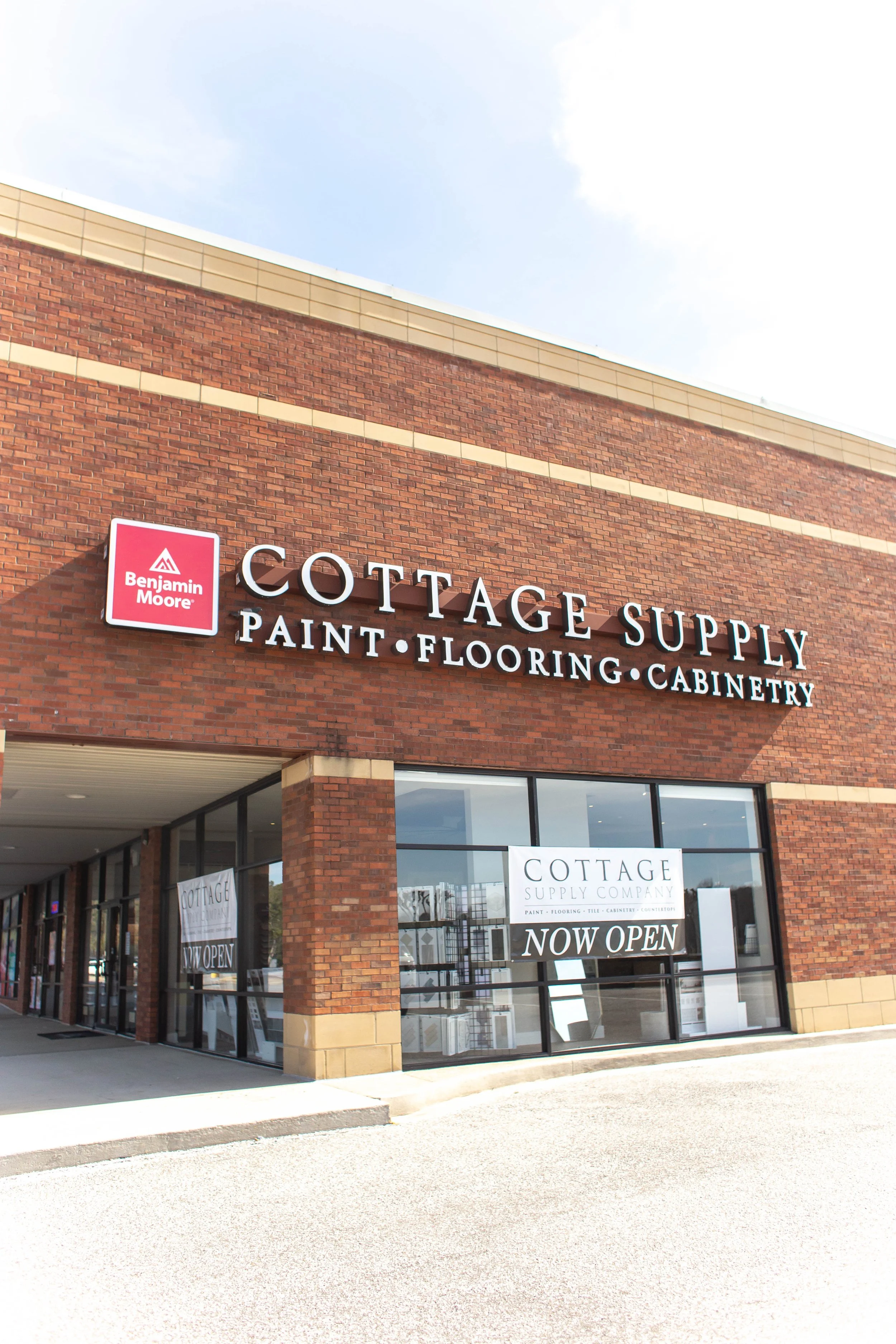 Cottage Supply storefront with Benjamin Moore sign, offering paint, flooring, and cabinetry products, with 'Now Open' signage in the window. Chelsea, AL