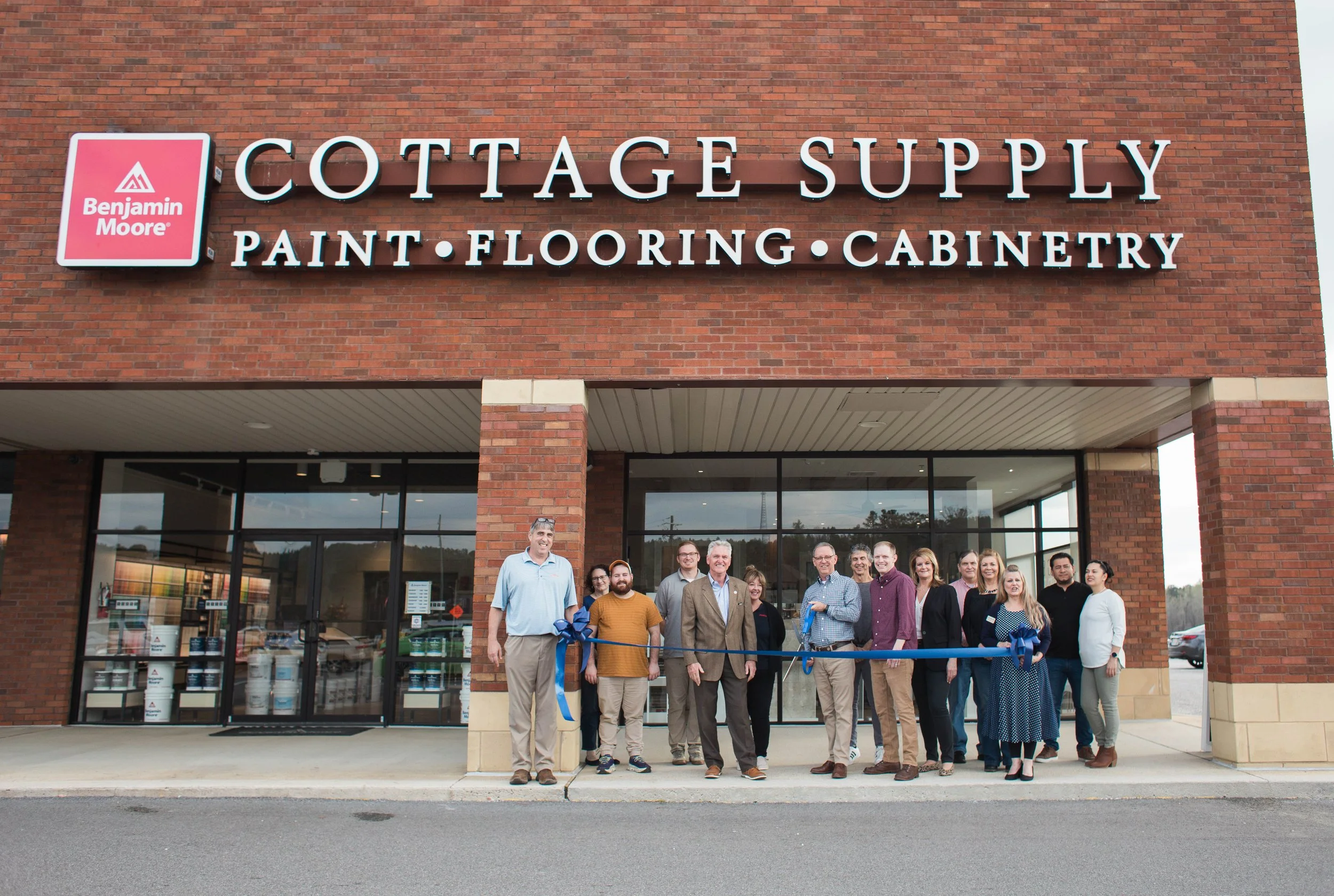 Group of people at ribbon-cutting ceremony in front of Cottage Supply store with Benjamin Moore products.