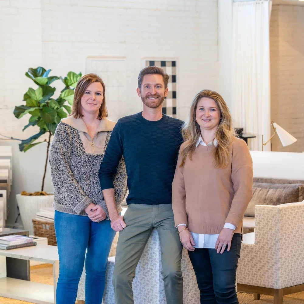 Three people standing indoors in a modern living room setting.