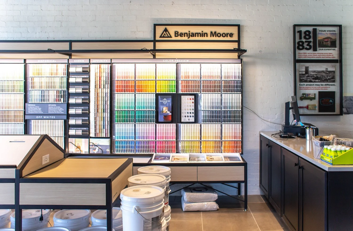 Interior of a Benjamin Moore paint store with color samples on display, buckets of paint on the floor, and a counter with supplies.