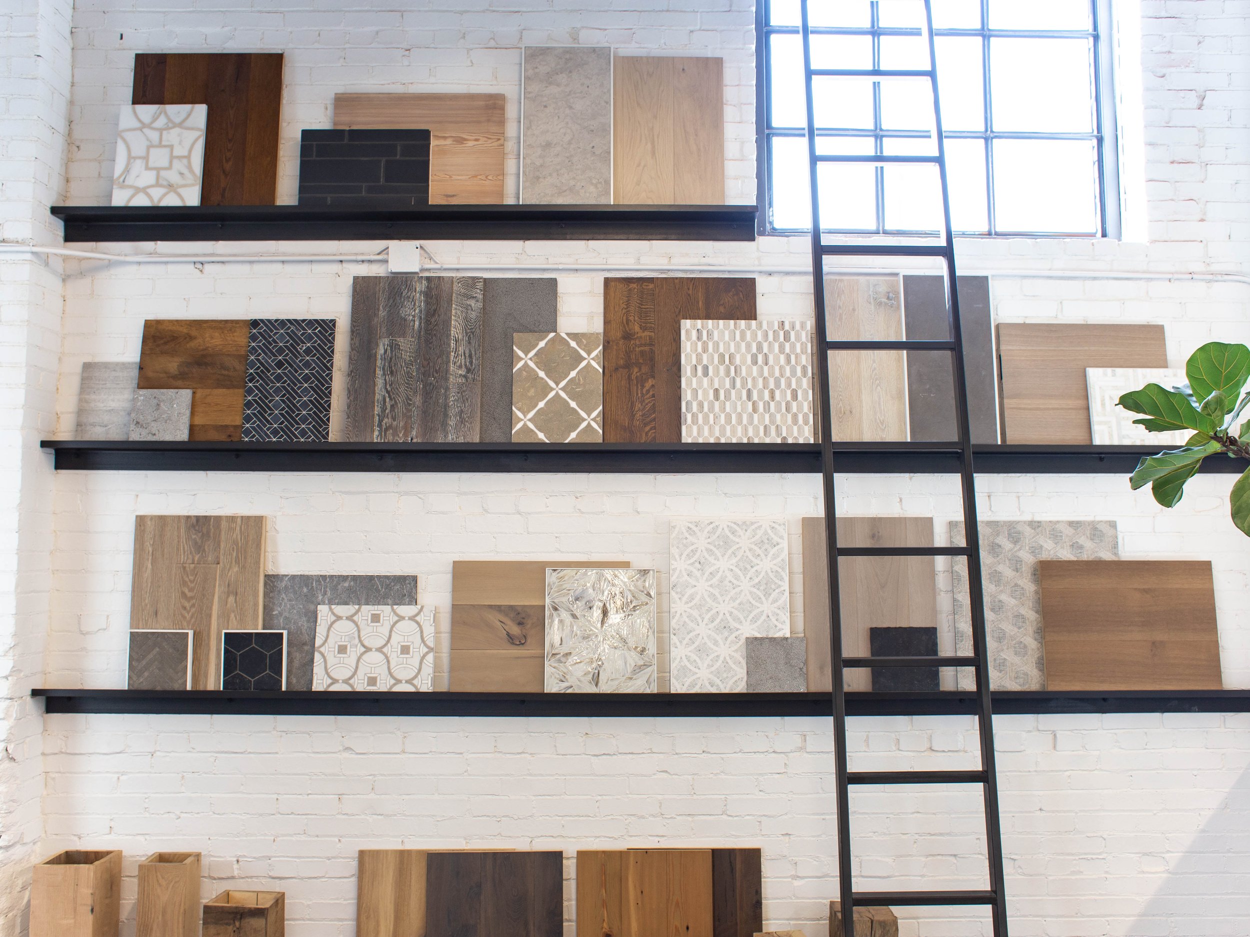 Wall displaying various flooring and tile samples on shelves with a ladder for access in a showroom.