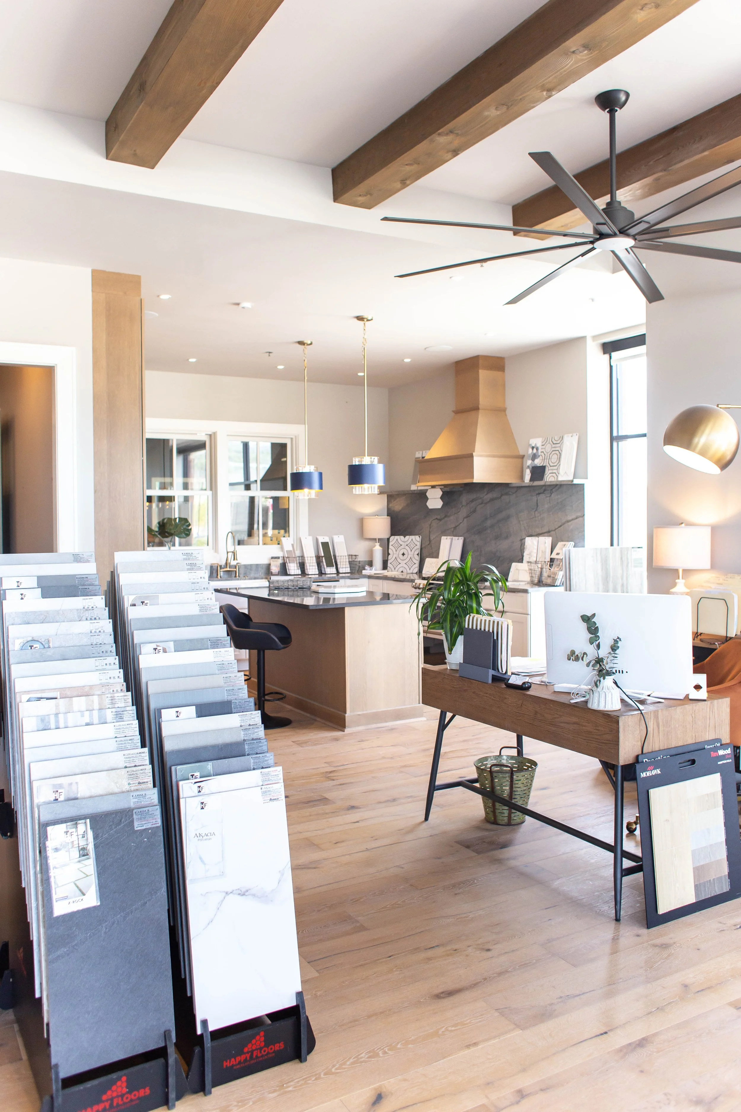 Interior view of a tile showroom with display racks, wooden flooring, sample tiles, a counter with pendant lights, and a ceiling fan. Chelsea, AL.