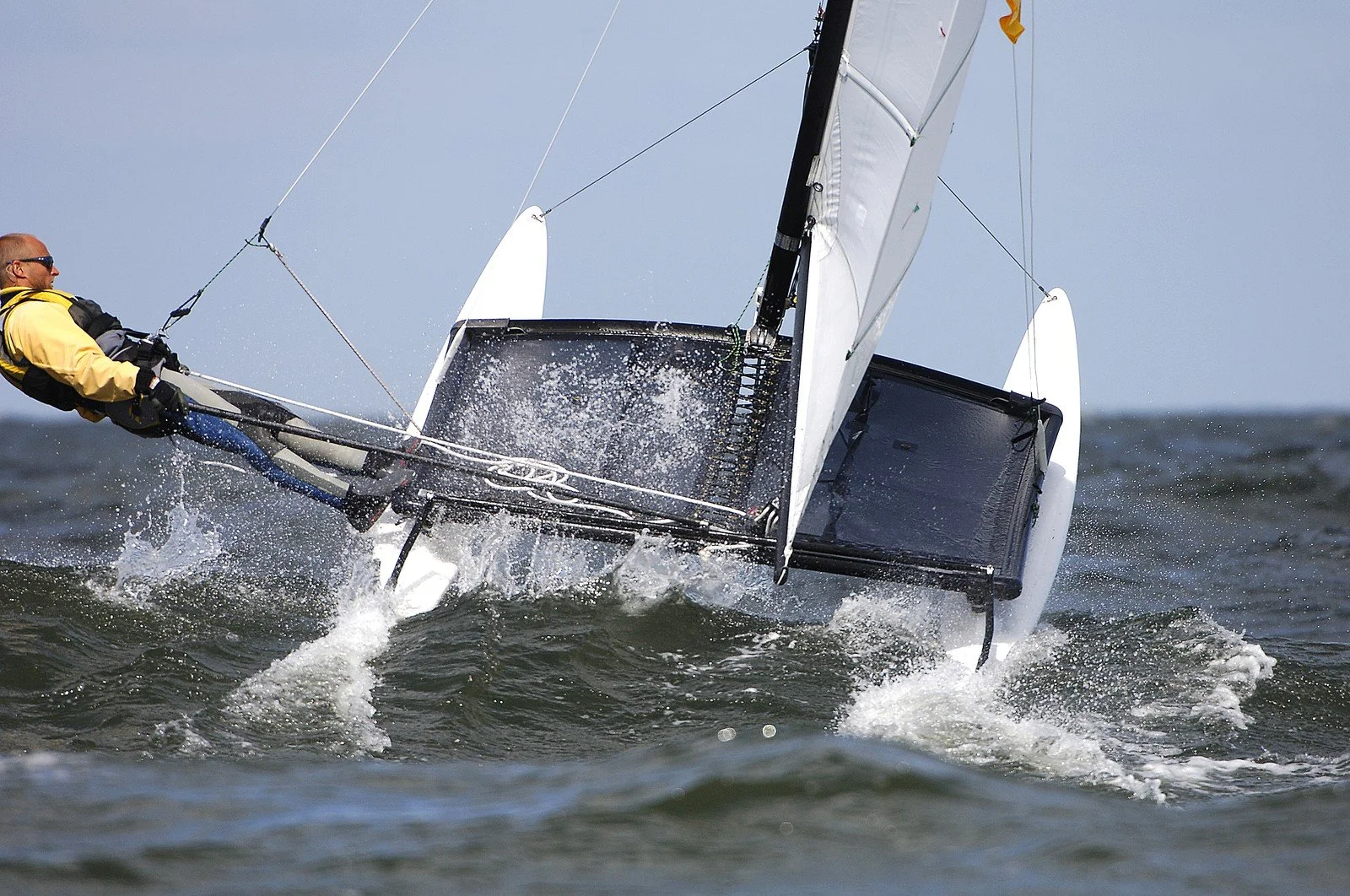 A catamaran is being sailed by someone over cresting waves