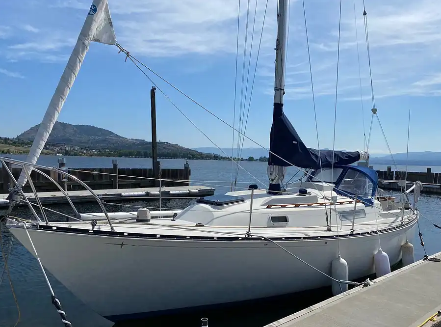 A white sailboat docked at a marina, with a mountain and body of water in the background.