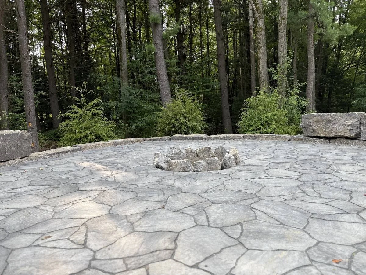Woodland paver patio with a boulder fire ring and stone block seating — Genesee Valley Landscape