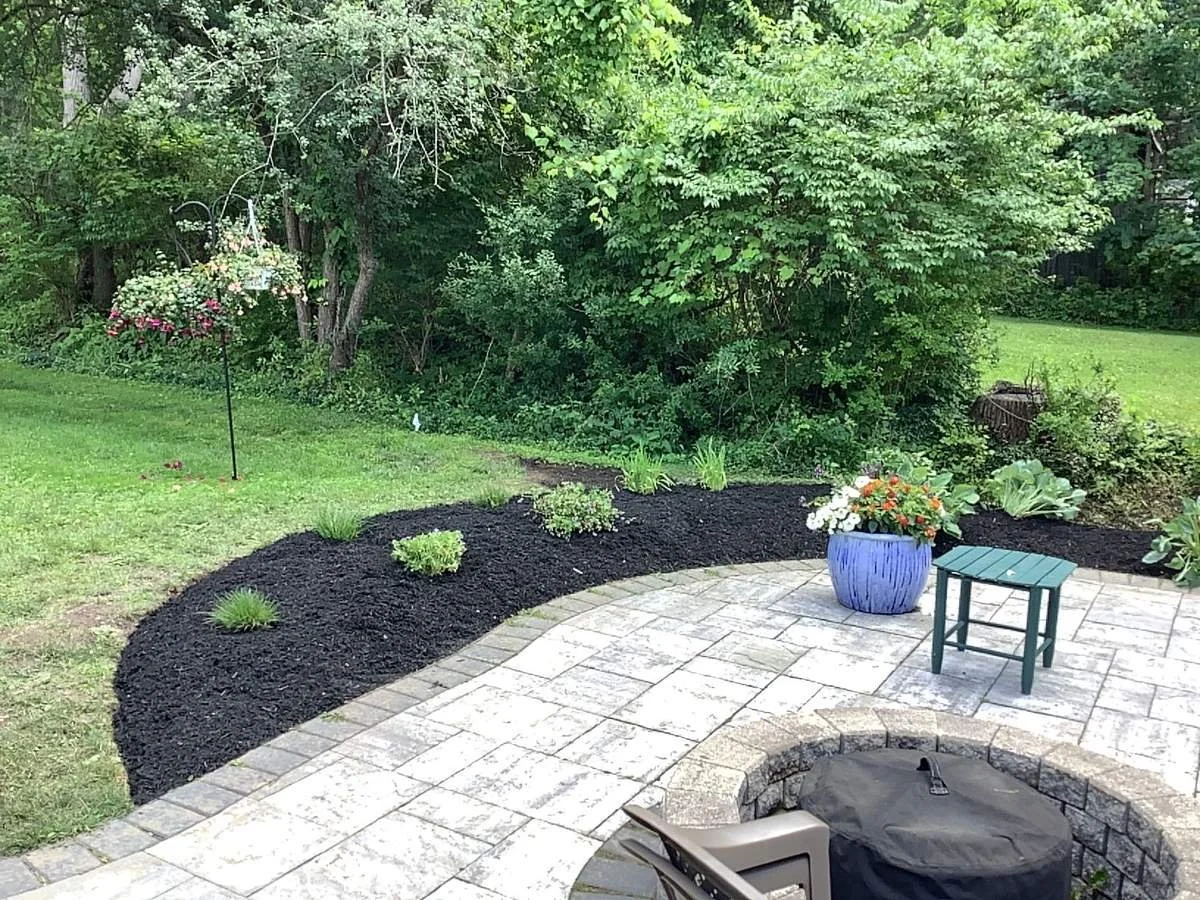 Curved planting bed with black mulch along a paver patio with a fire pit — Genesee Valley Landscape