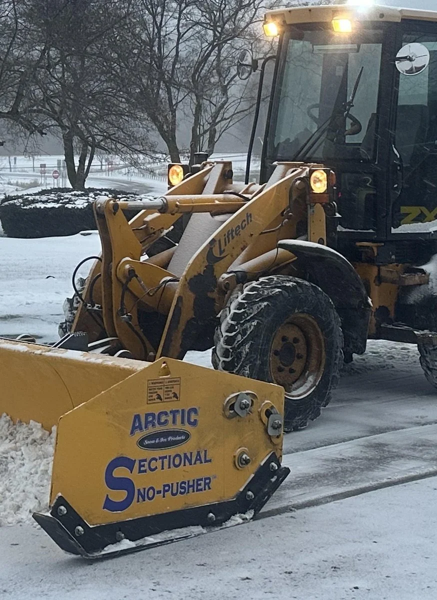 Loader with sectional snow pusher clearing a commercial parking lot in Livingston County, NY