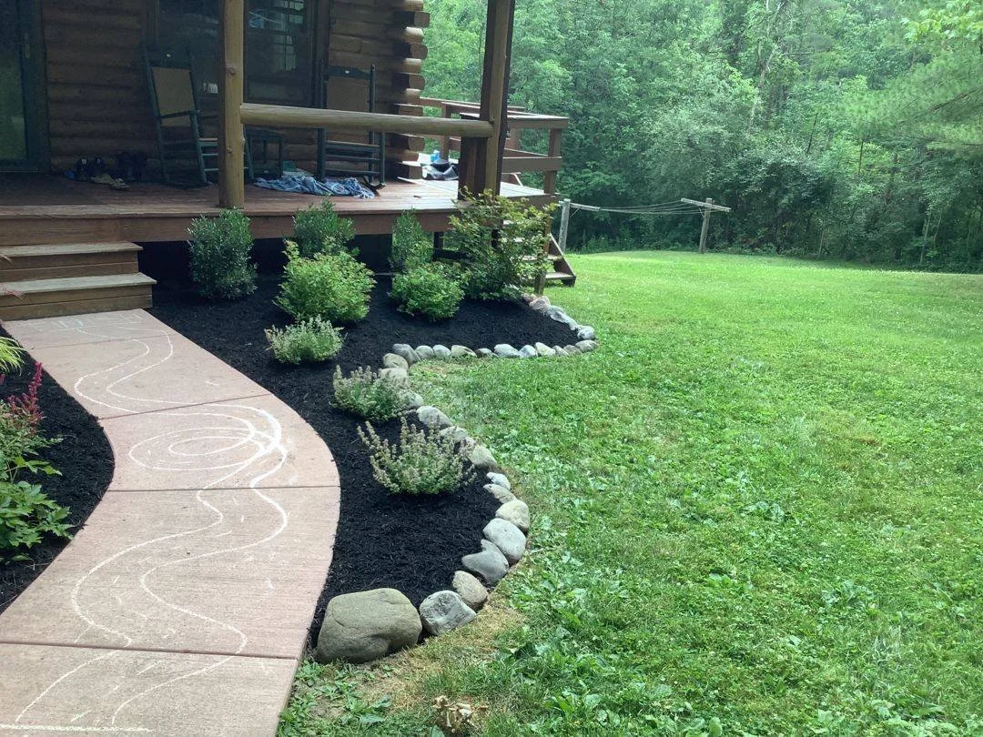 River rock edged planting bed beside a concrete walk and log home porch — Genesee Valley Landscape