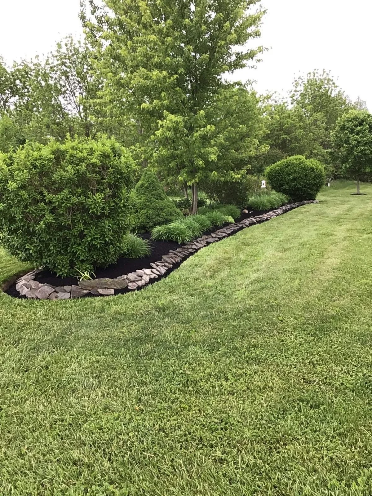 Freshly mowed lawn along a stone-edged bed with daylilies, shrubs and black mulch — Genesee Valley Landscape