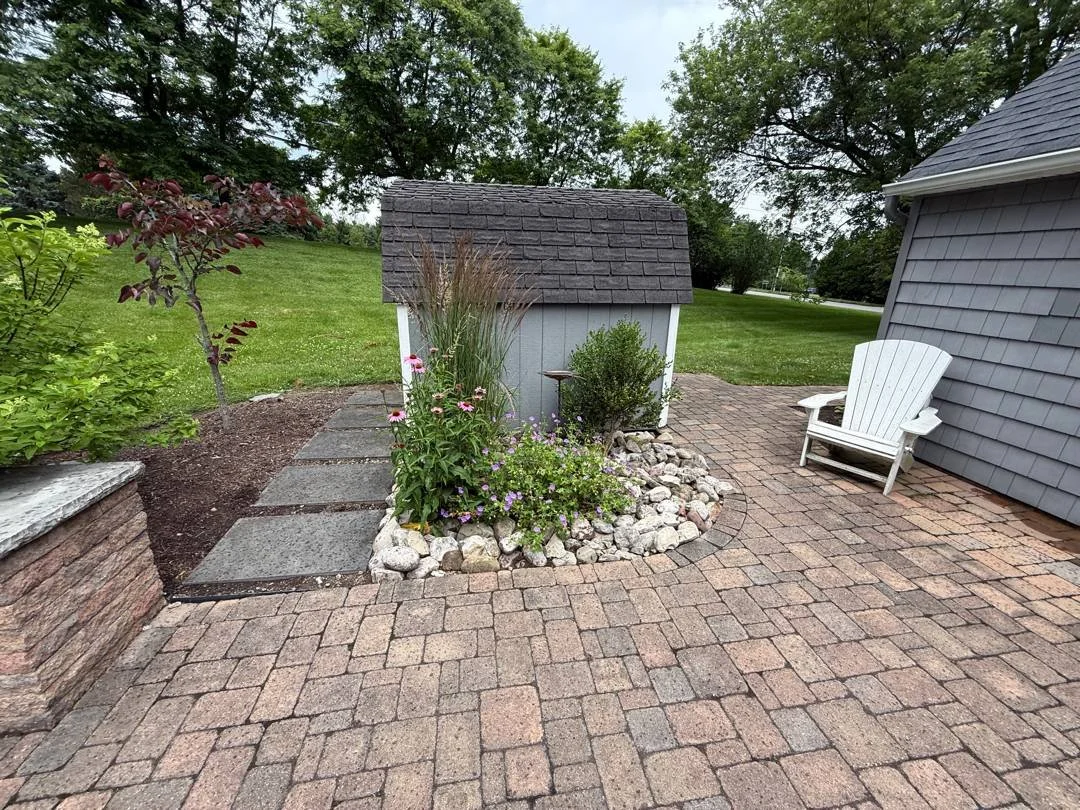 Brick paver patio with a stone stepping path and river rock edged flower bed — Genesee Valley Landscape
