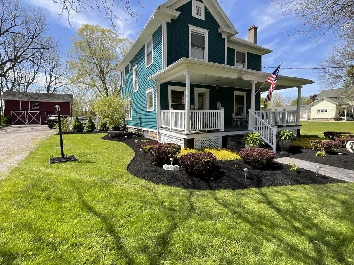 Fresh black mulch beds with barberry and golden shrubs around a teal farmhouse porch — Genesee Valley Landscape