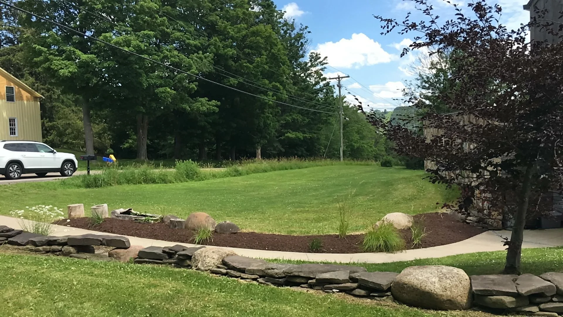 Mulched bed with boulders and ornamental grasses behind a dry stacked stone wall — Genesee Valley Landscape