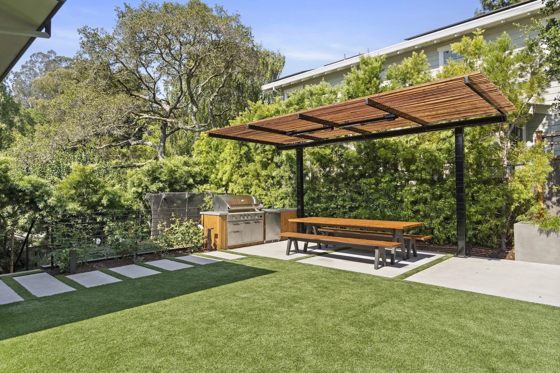 Wooden pergola, plantings and outdoor kitchen with wooden picnic table