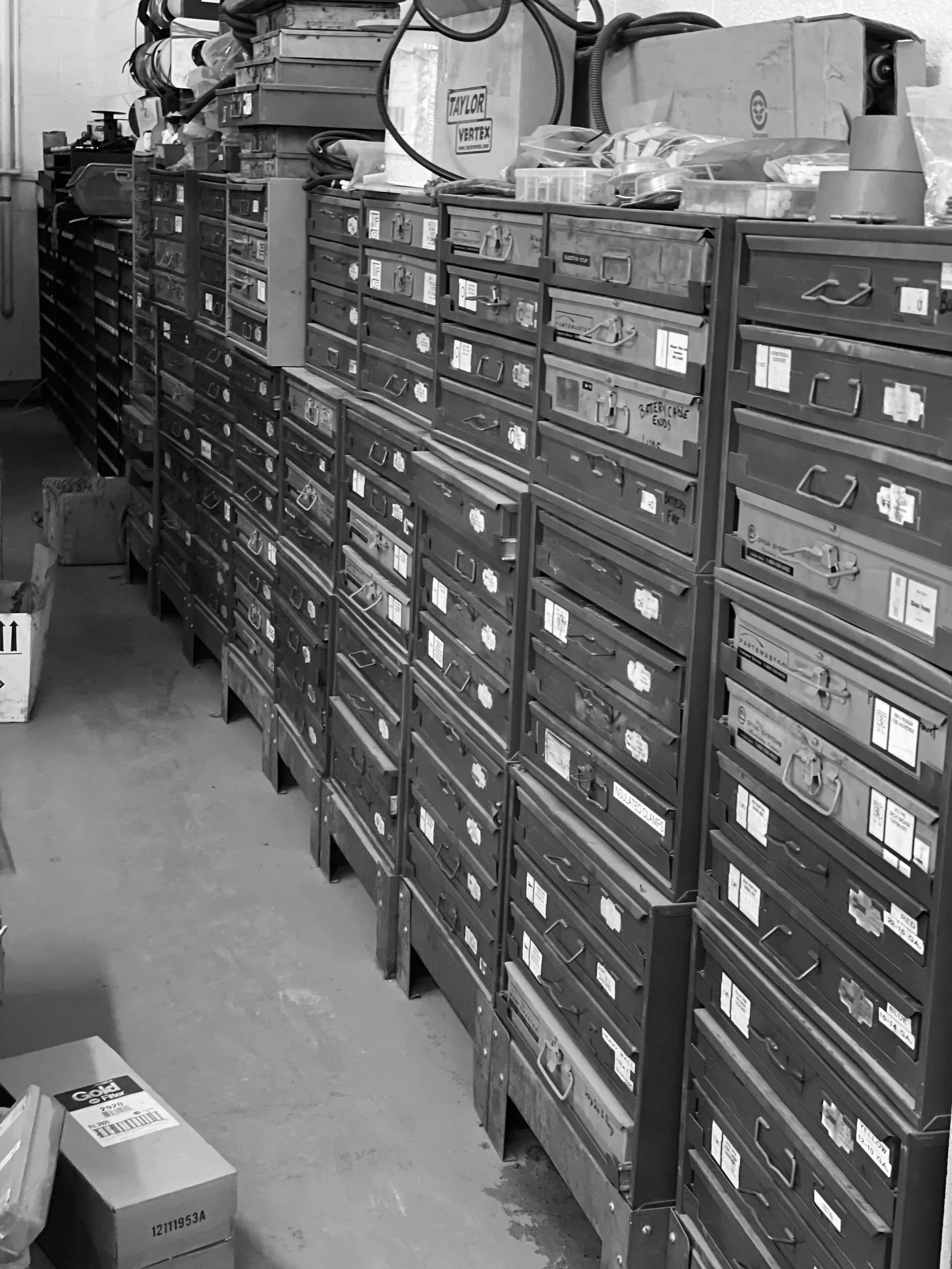 A storage area with organized metal drawers containing small parts or tools, along with a few loose items like boxes and bags on the floor and on top of the cabinets.