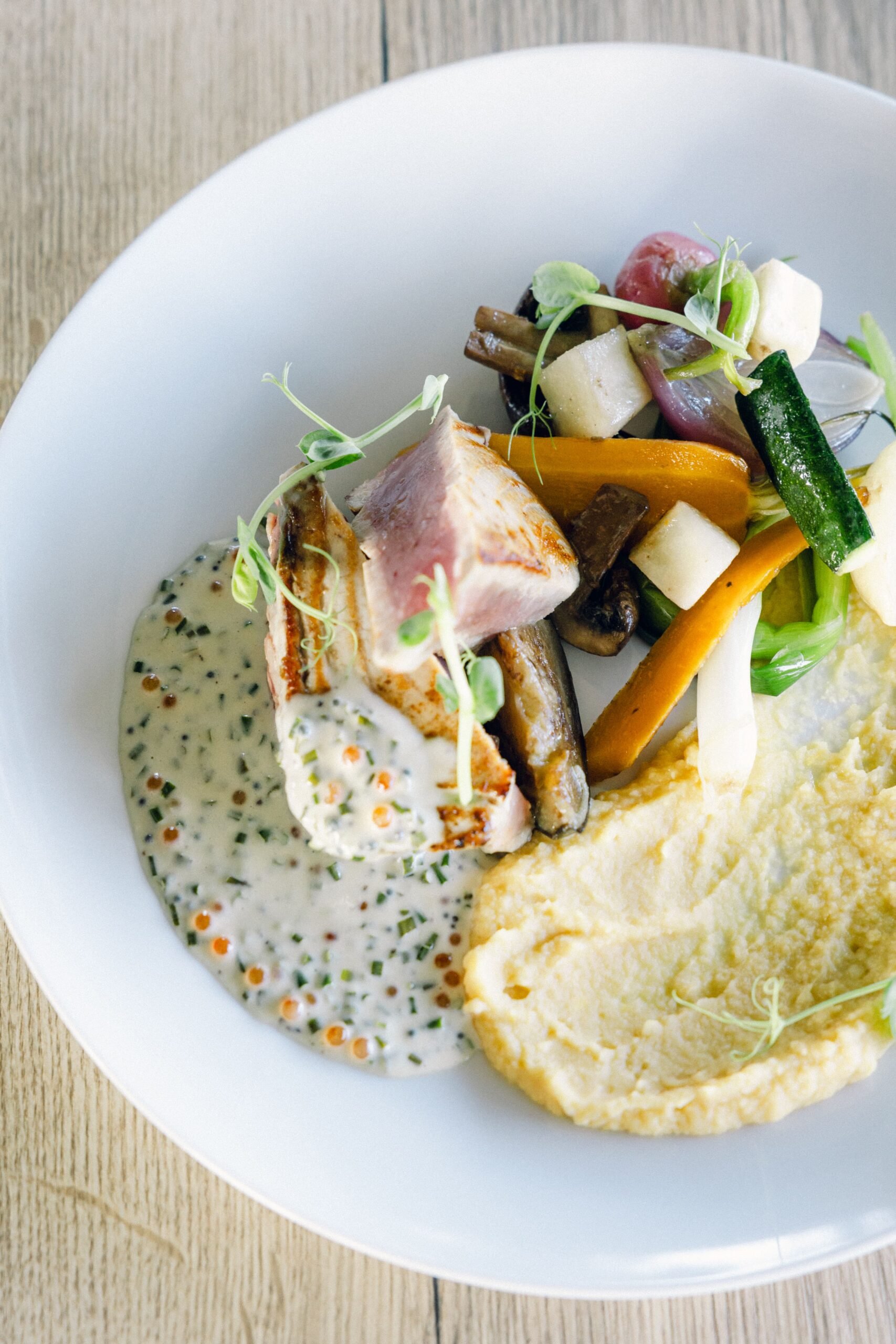 Plat gastronomique avec poisson grillé, sauce crémeuse aux herbes, purée et légumes variés.