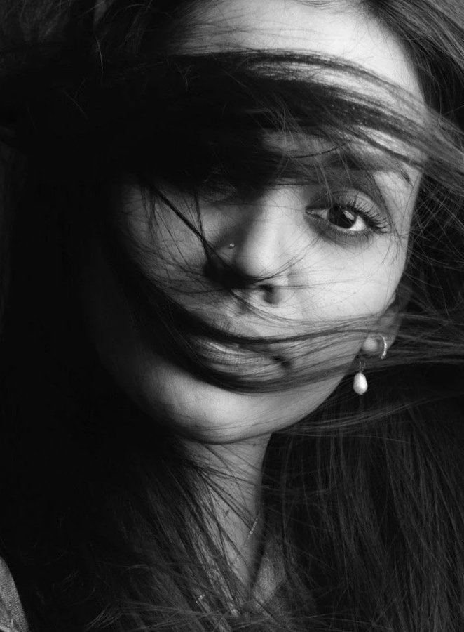 Portrait en noir et blanc d'une femme avec des cheveux longs et ébouriffés, portant une chemise en jean, passant la main dans ses cheveux, regardant vers l'objectif.