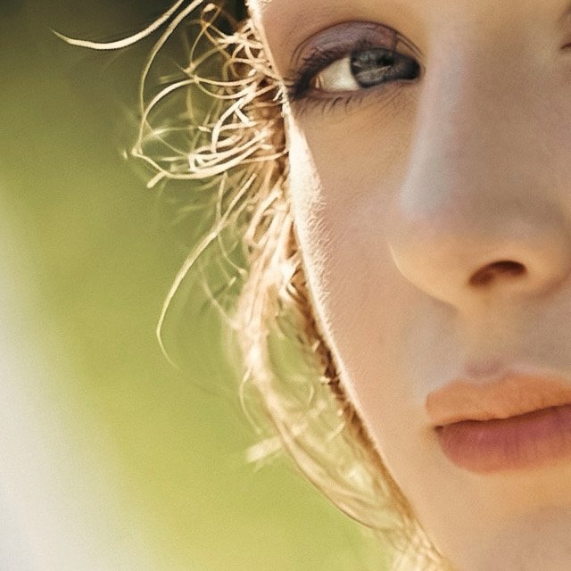 Une femme avec des cheveux bouclés, portant des bijoux et une robe satinée, repose sur un sol brillant.