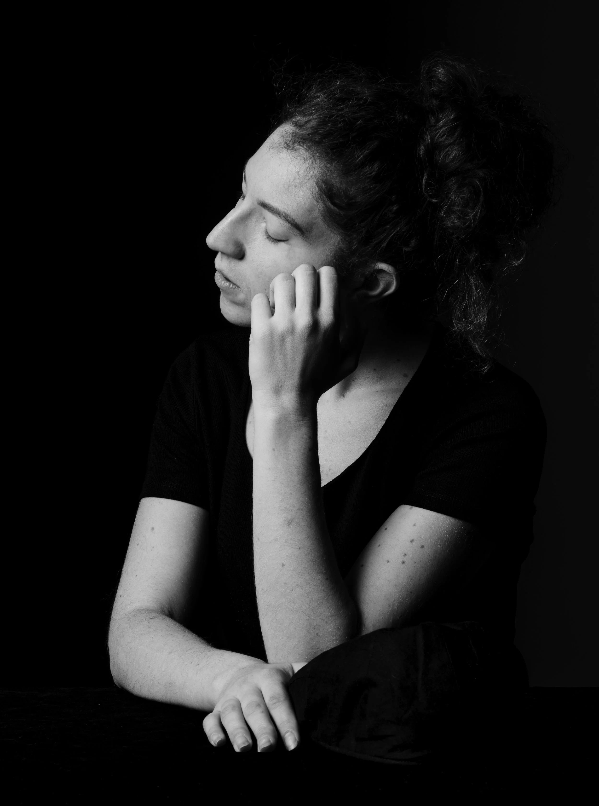 Femme posant en noir et blanc, tête penchée, yeux fermés.