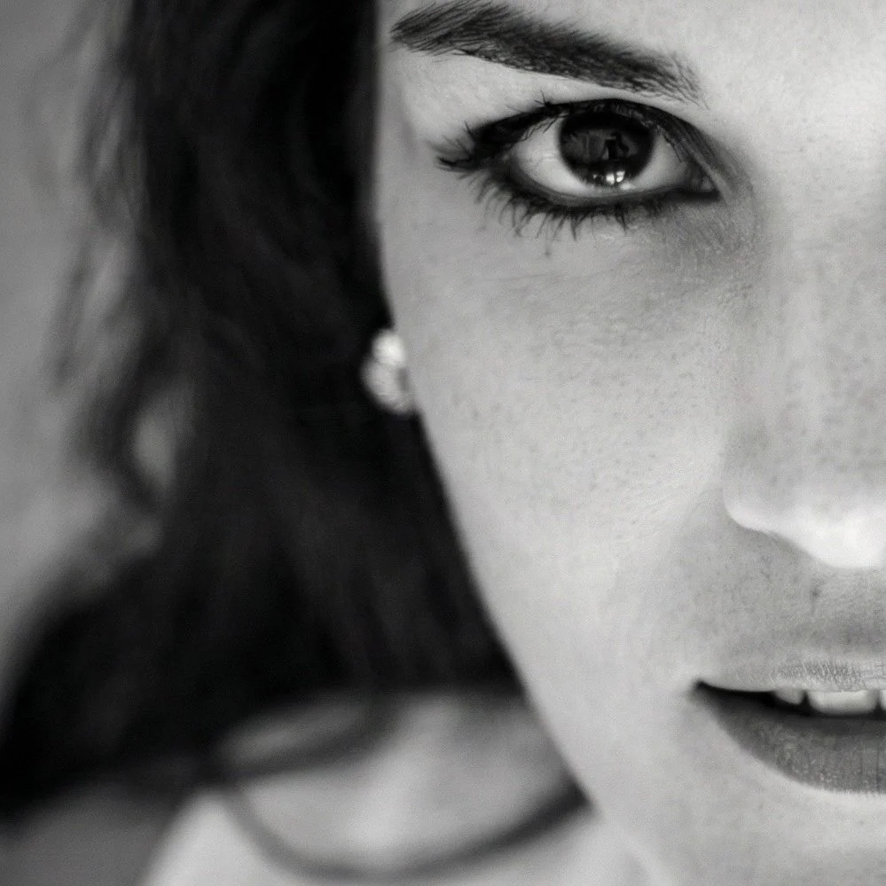 Portrait en noir et blanc d'une femme avec des yeux expressifs, portant des boucles d'oreilles et un collier, regardant vers l'appareil.