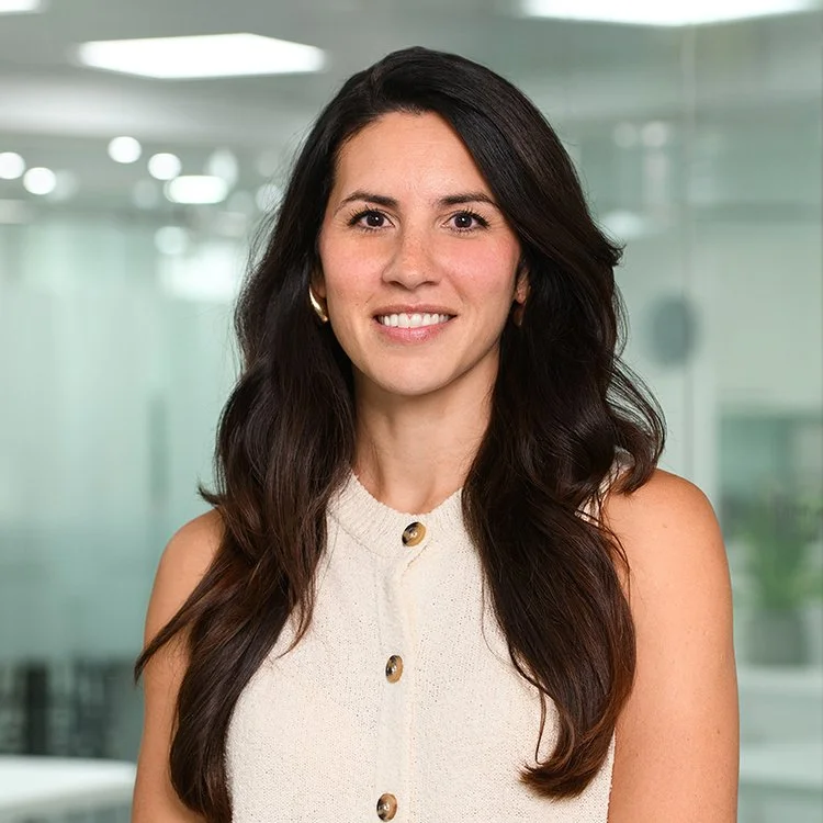 A woman with long, dark brown hair smiling in an office environment.