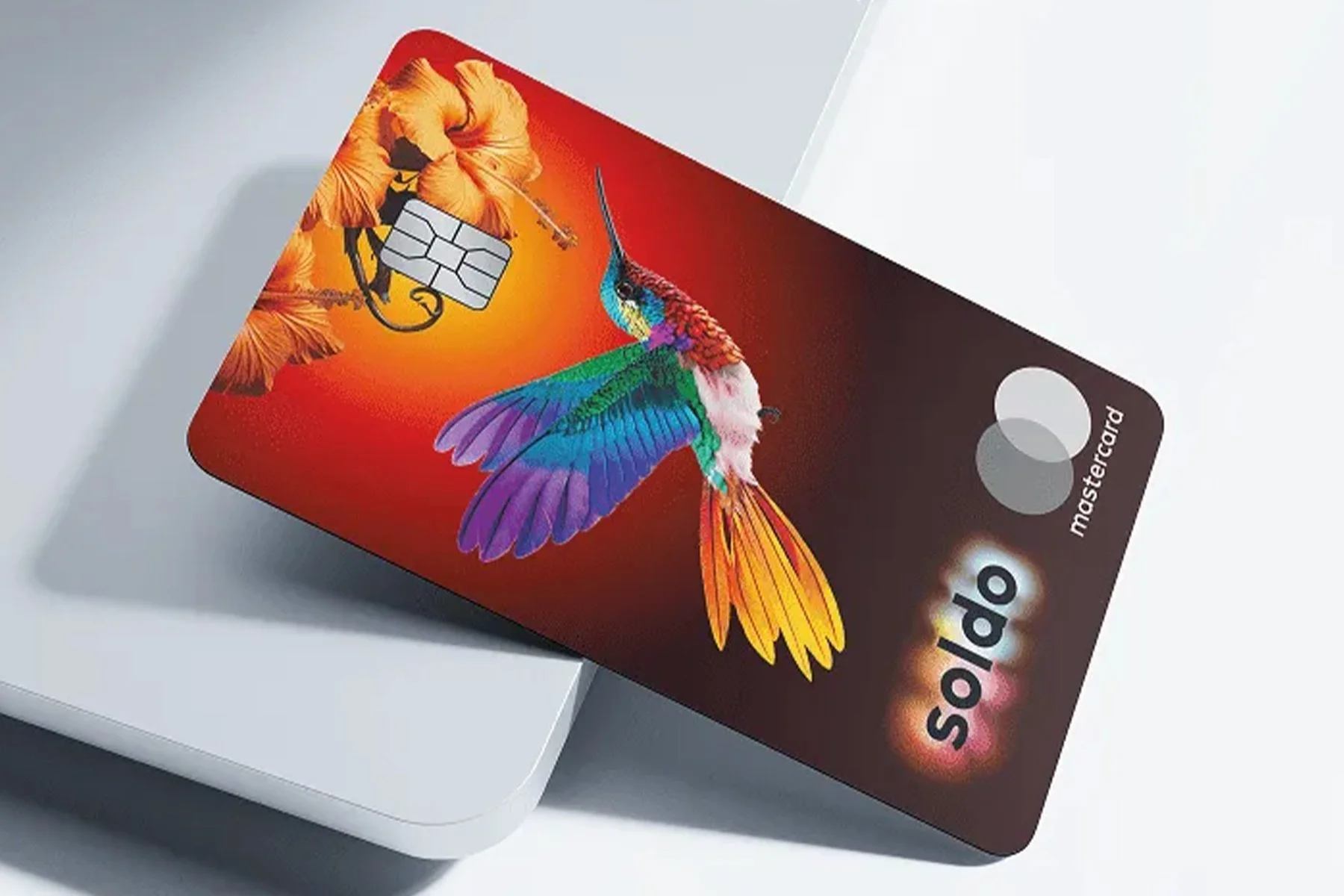 Close-up of a Mastercard credit card featuring a colorful hummingbird and orange flowers on a red background.