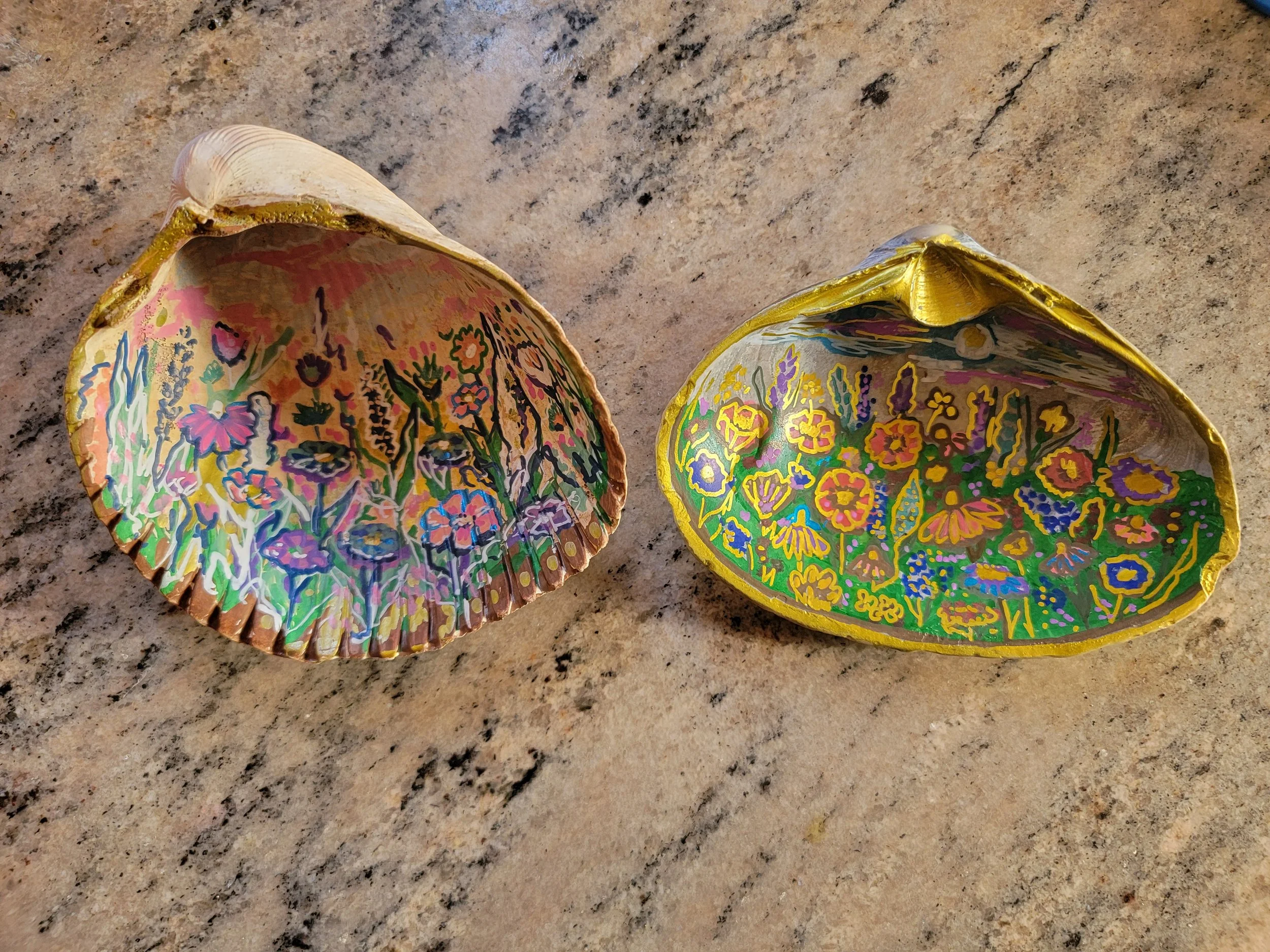 Two decorated seashells with floral designs inside, placed on a stone surface.