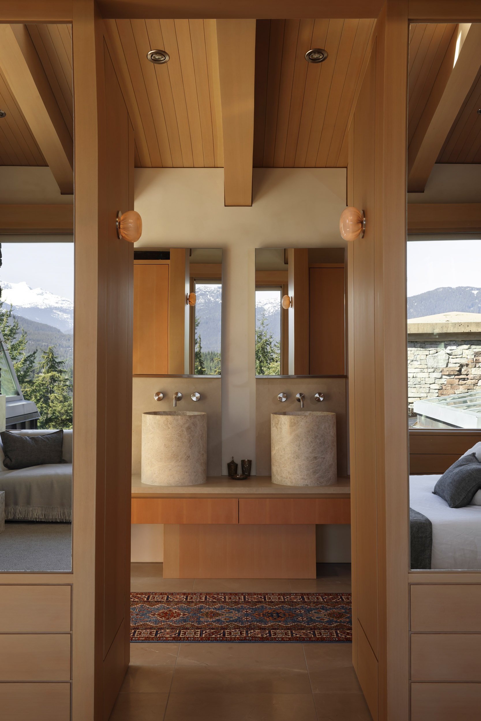 View of a modern bathroom with two stone vessel sinks, mirrors, and mountain views outside.
